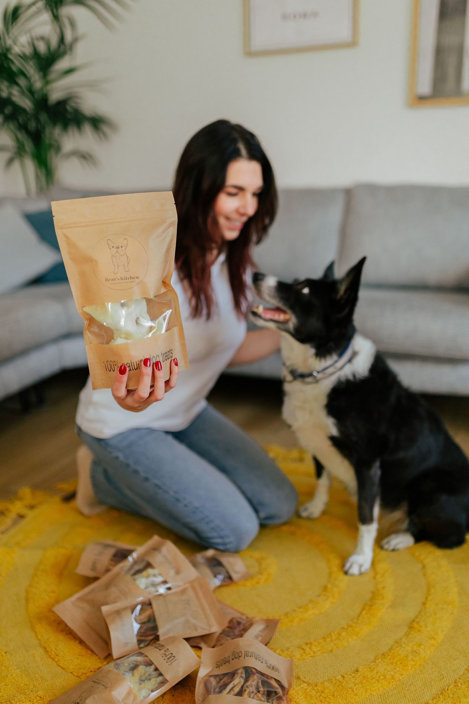 Dog treats in brown paper bags scattered on yellow rug with indoor plants in background.