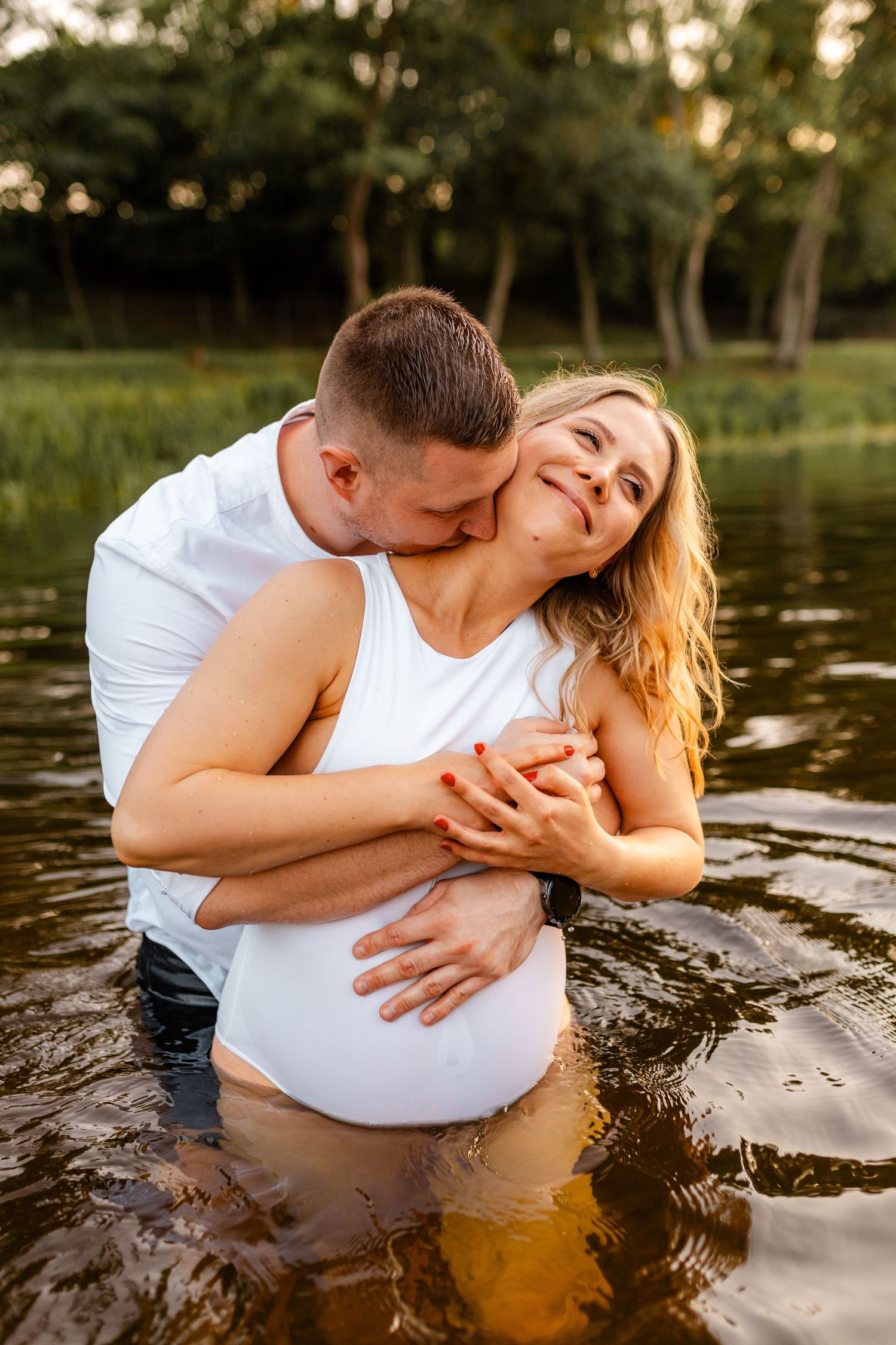 A couple embraces while standing in shallow water during sunset, creating a romantic atmosphere.