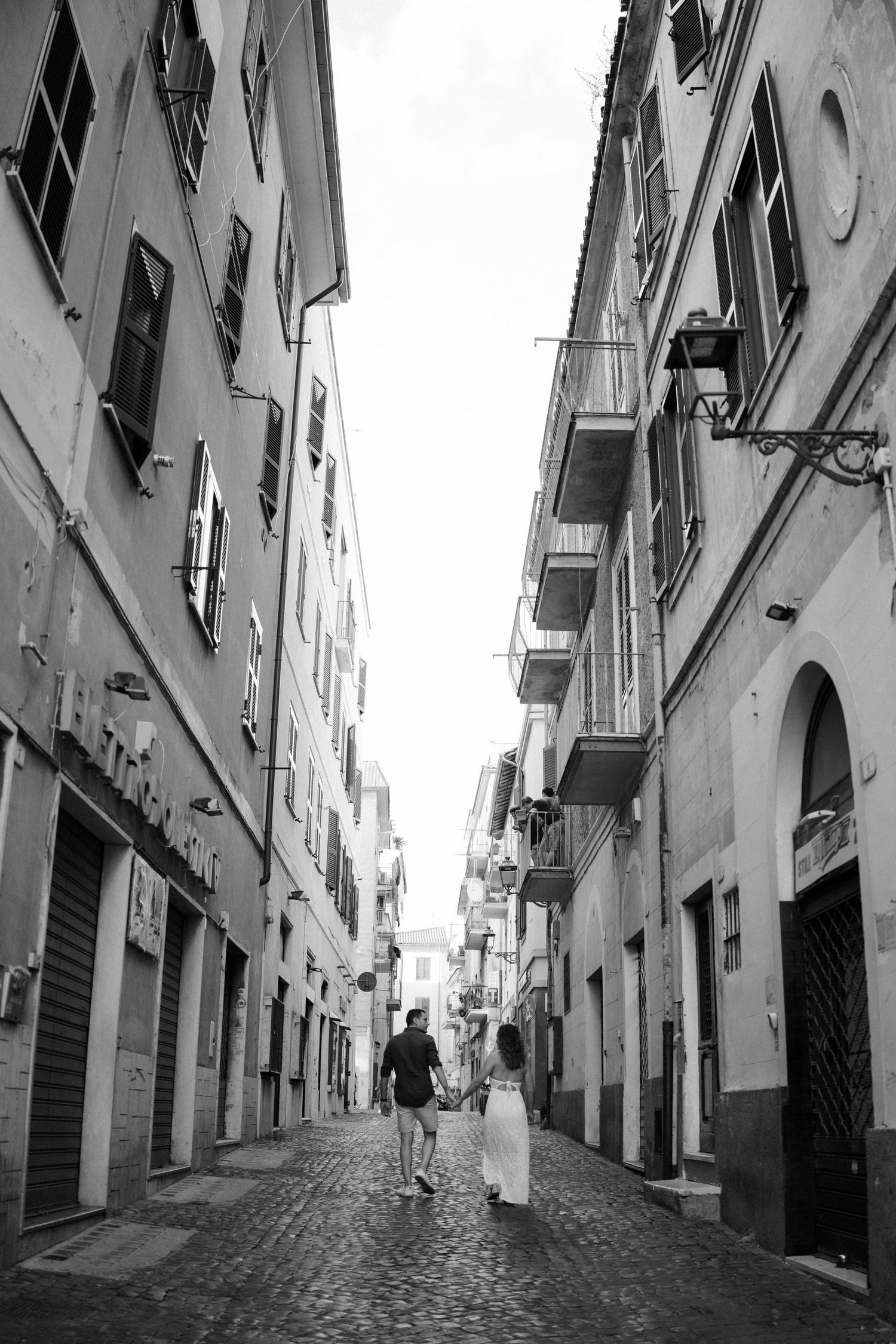 Black and white photos of a narrow cobblestone alley between historic buildings with balconies.