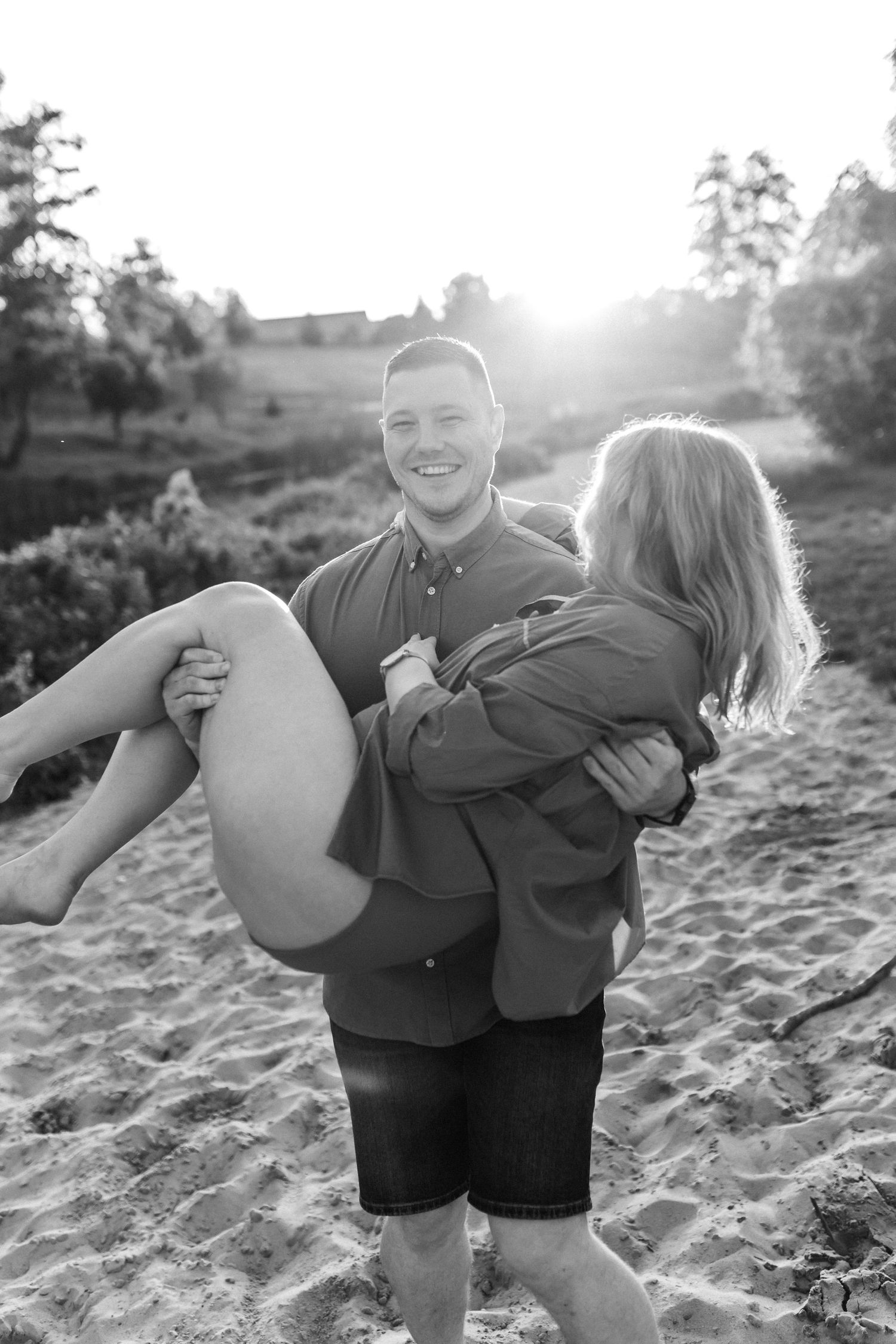 Black and white beach photos of playful couple during sunset maternity session.