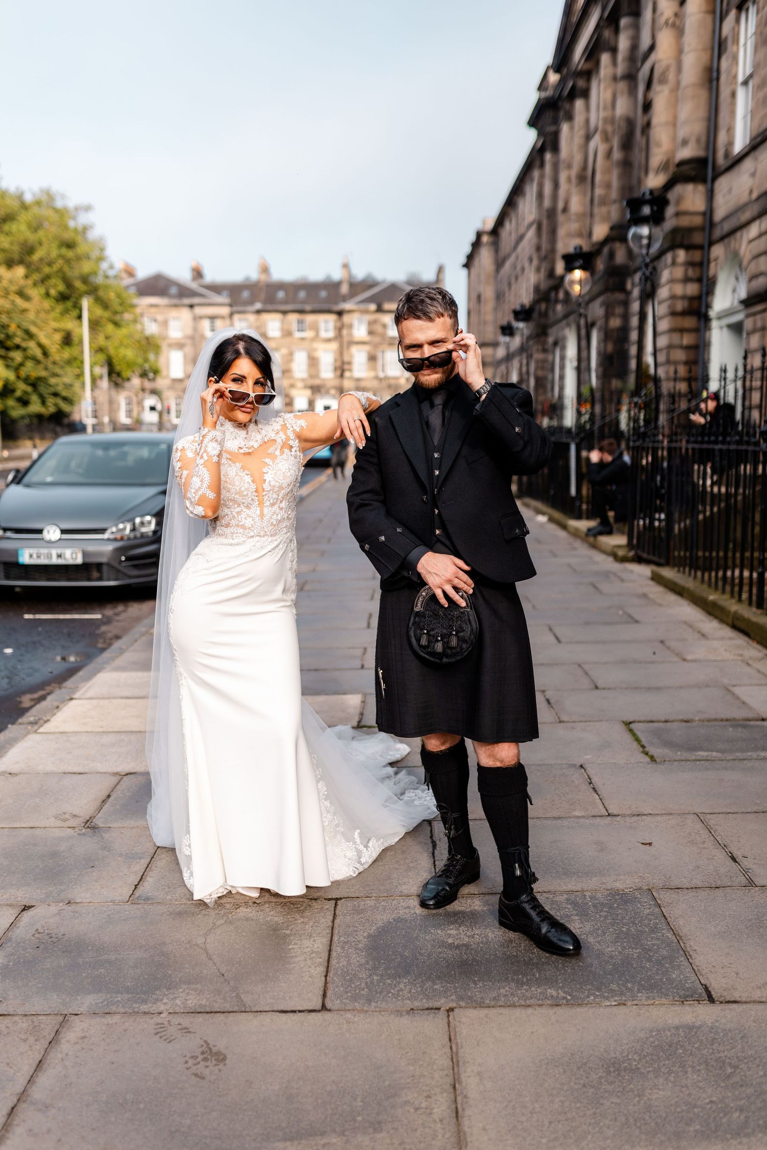 Wedding couple in white dress and traditional Scottish kilt posing on Edinburgh street.