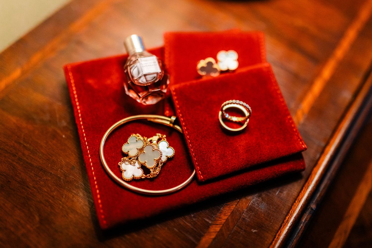 Wedding rings and jewelry displayed on red velvet cushion in warm lighting.