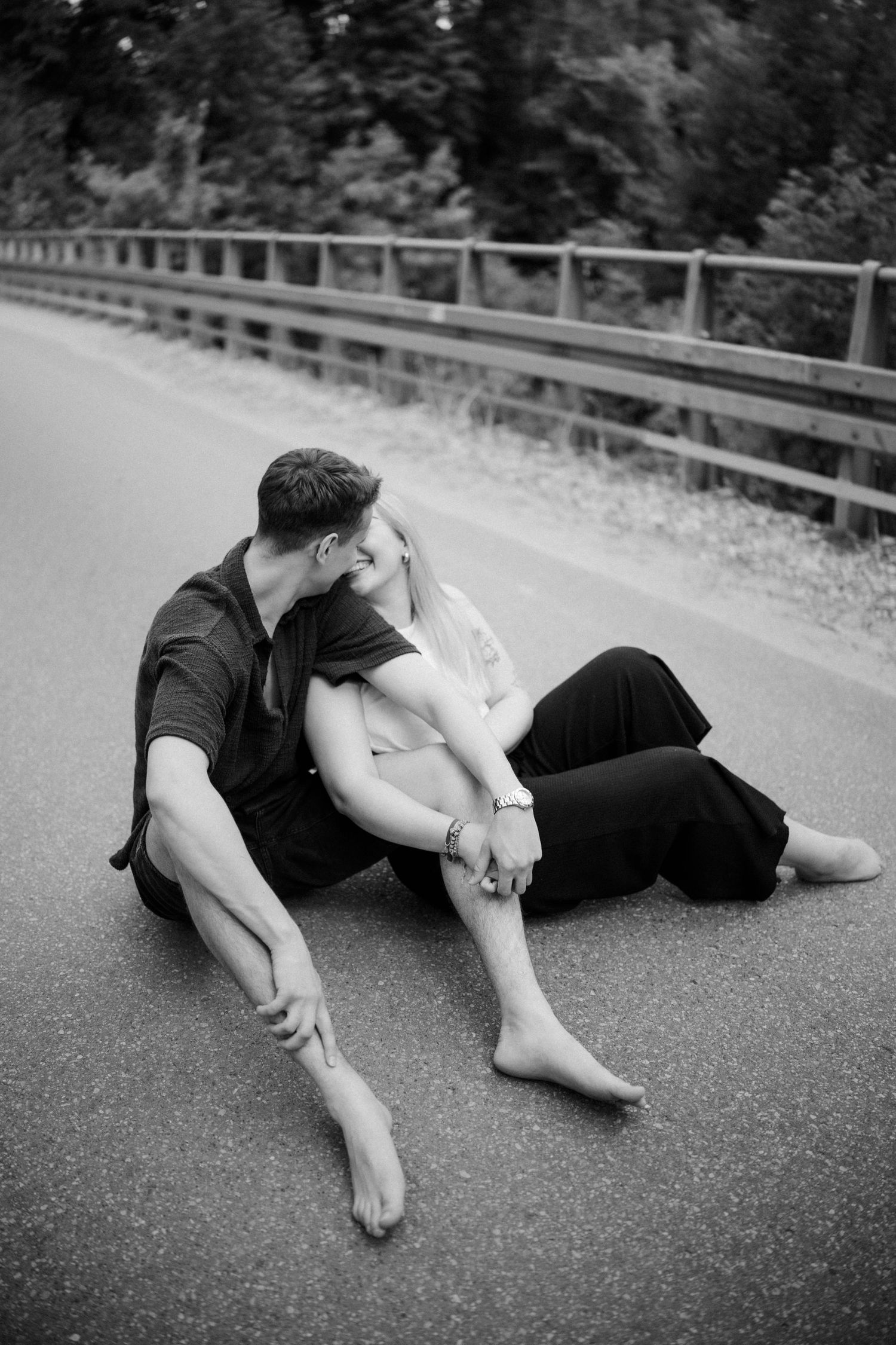 Two people lie together on asphalt road in artistic black and white composition.
