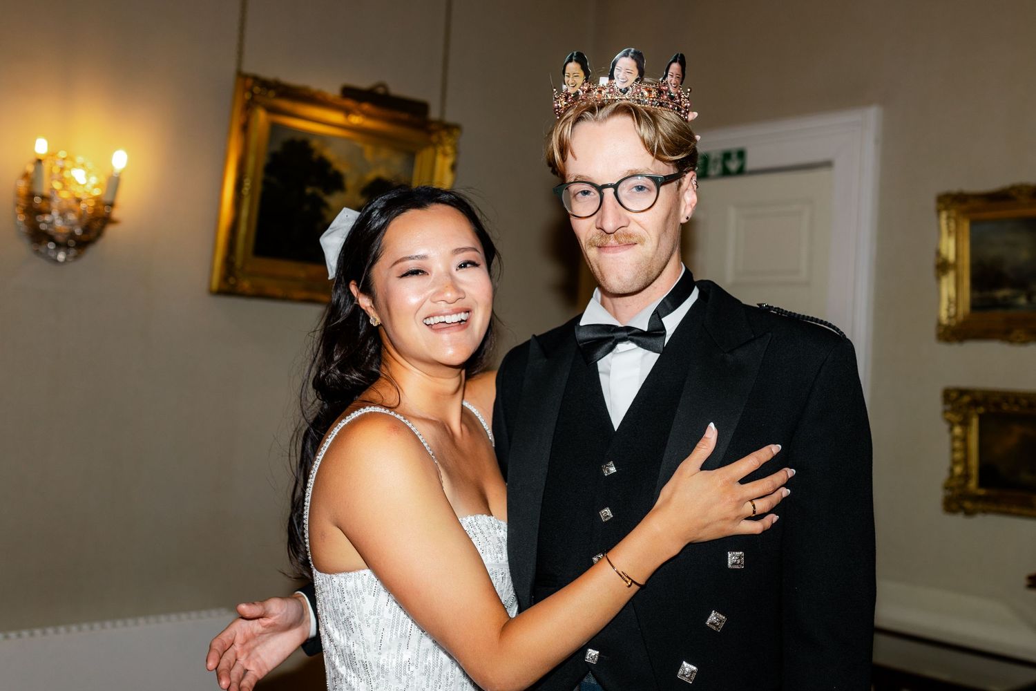 Wedding celebration in a formal room with ornate gold frames and elegant lighting.