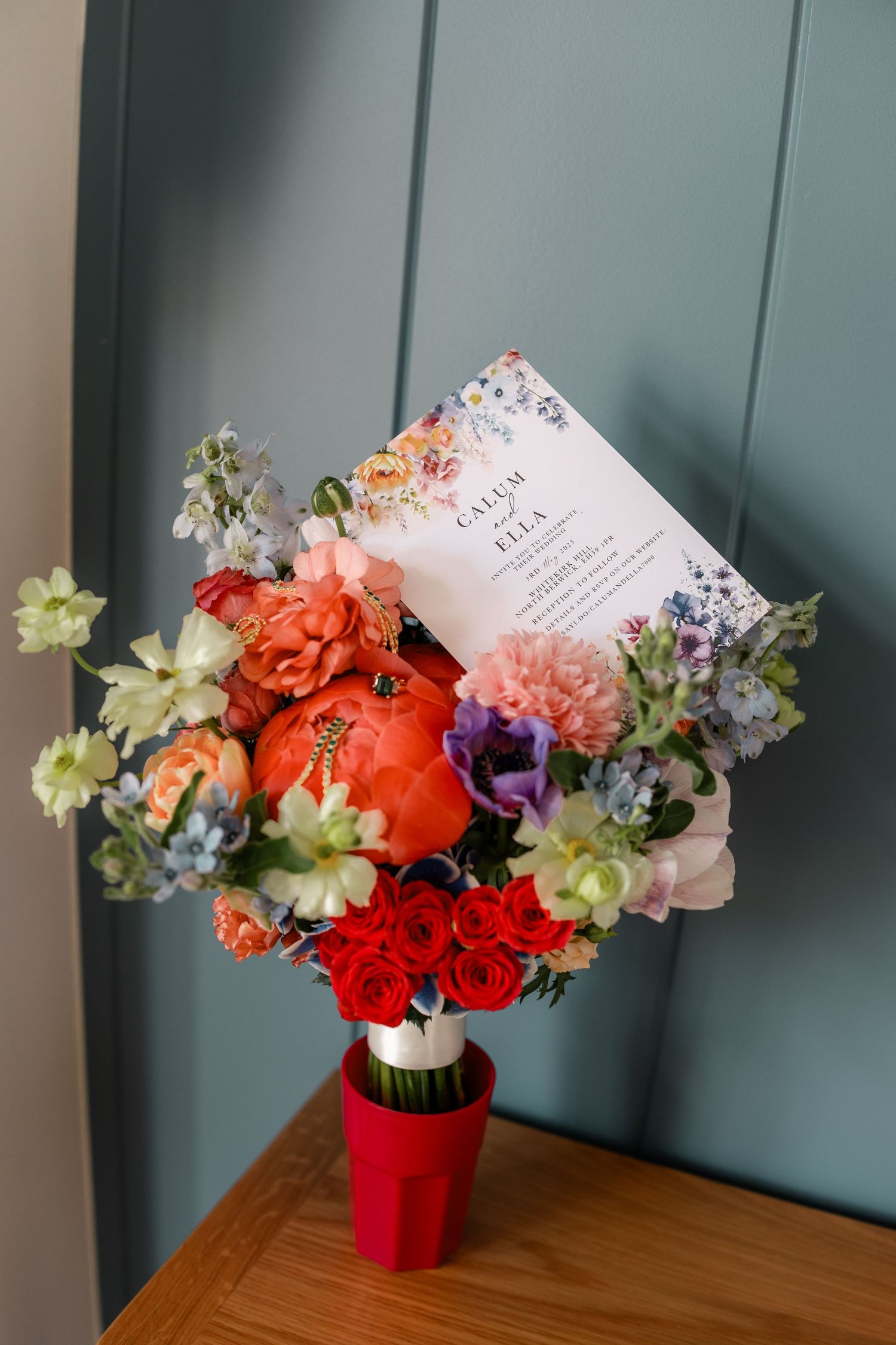 Colorful floral arrangements with red and pink blooms displayed on wooden table against blue wall.