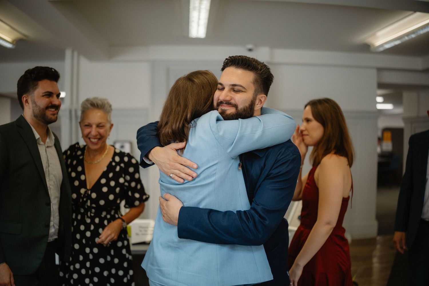 People embrace and celebrate together in a bright indoor office or event space.