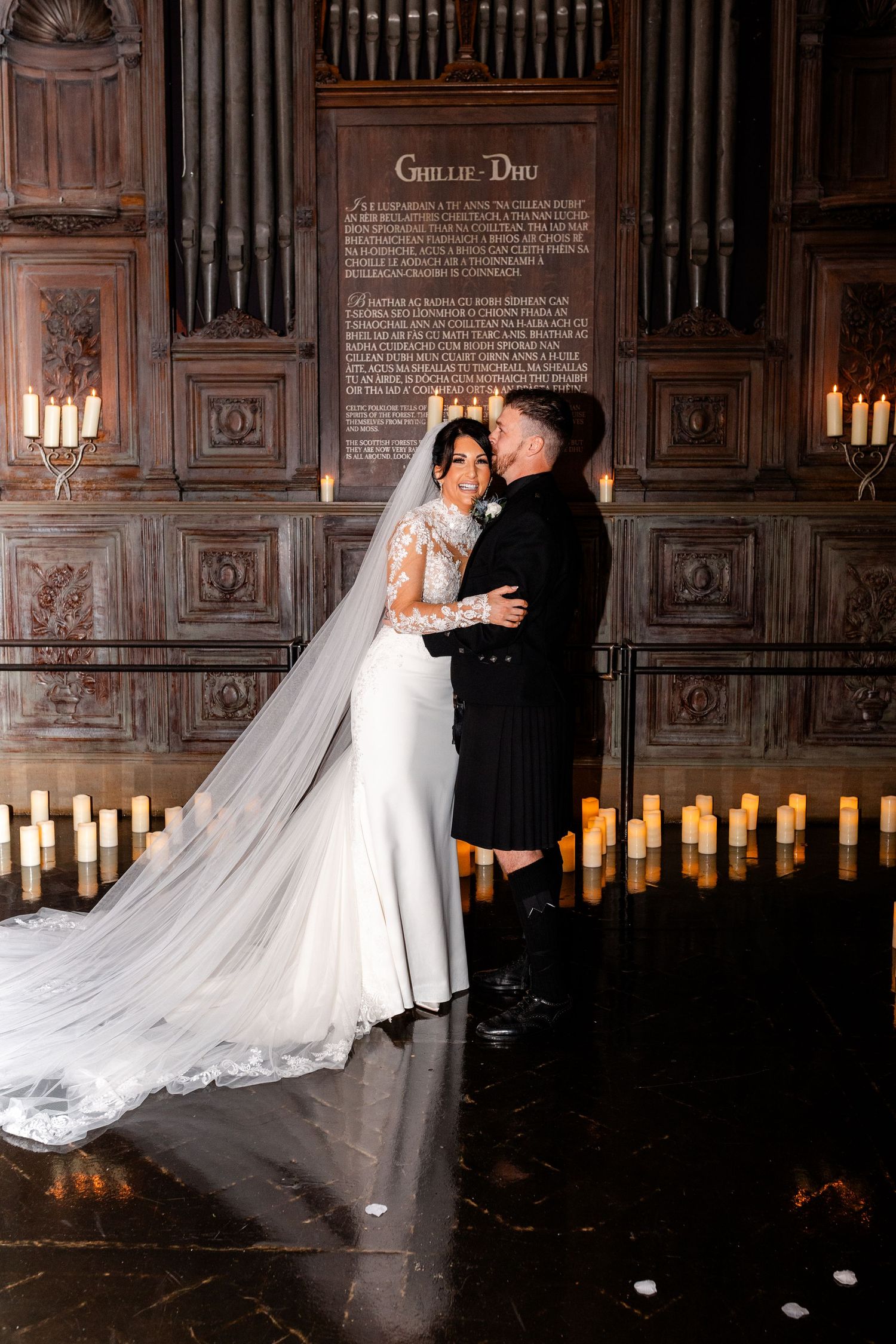 A couple shares a romantic dance moment in an elegant candlelit venue with ornate wood paneling and glowing candles.