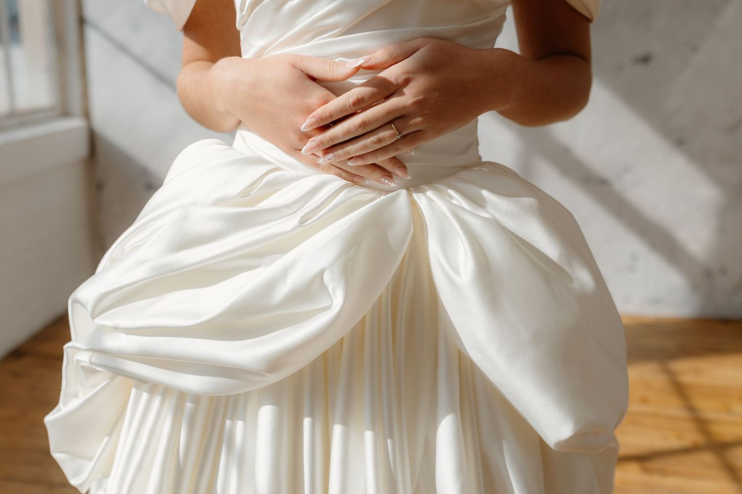 Bride in elegant white satin ball gown wedding dress, hands gracefully placed on waist, soft natural lighting.