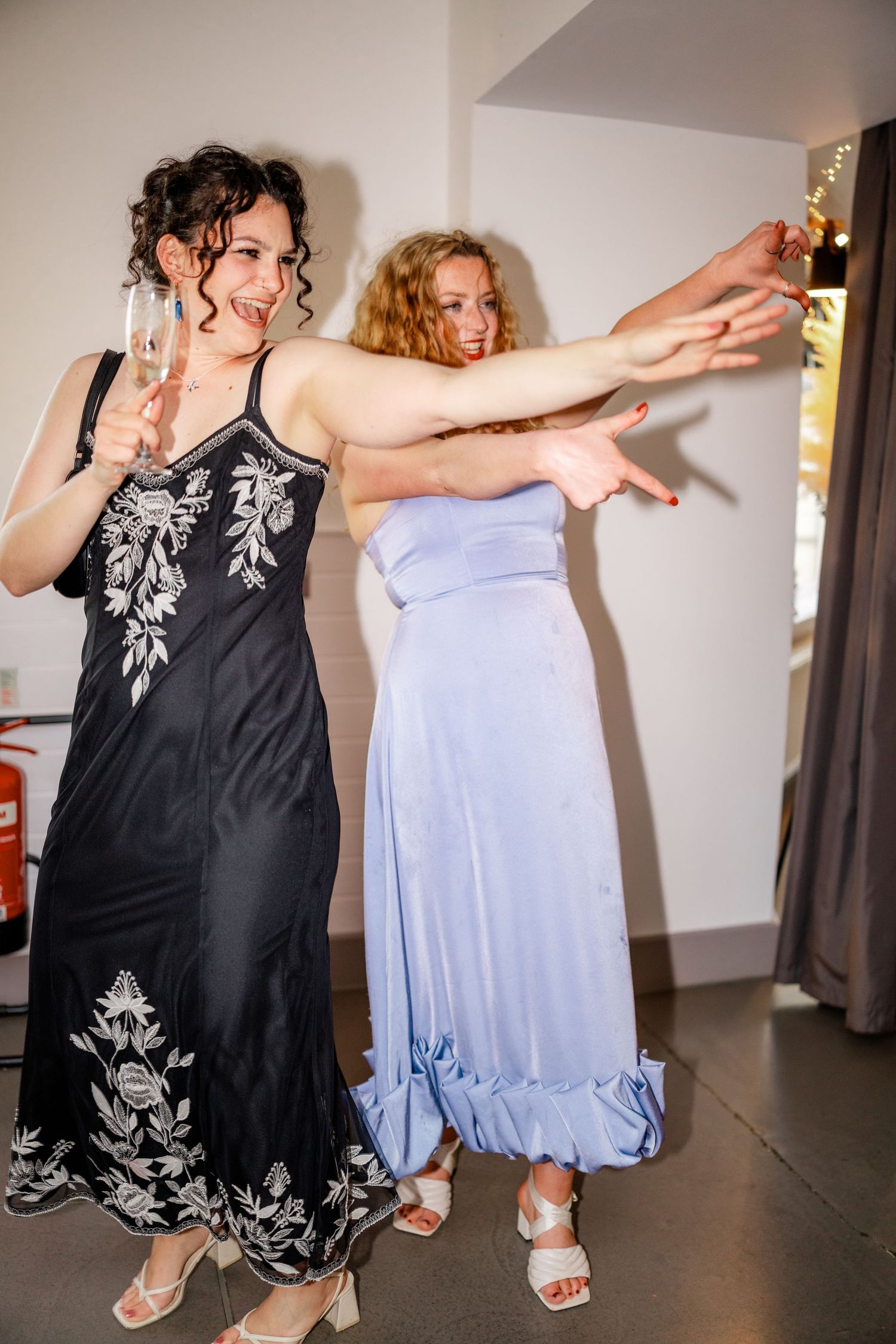Two women in elegant dresses dance and celebrate joyfully at a wedding reception.