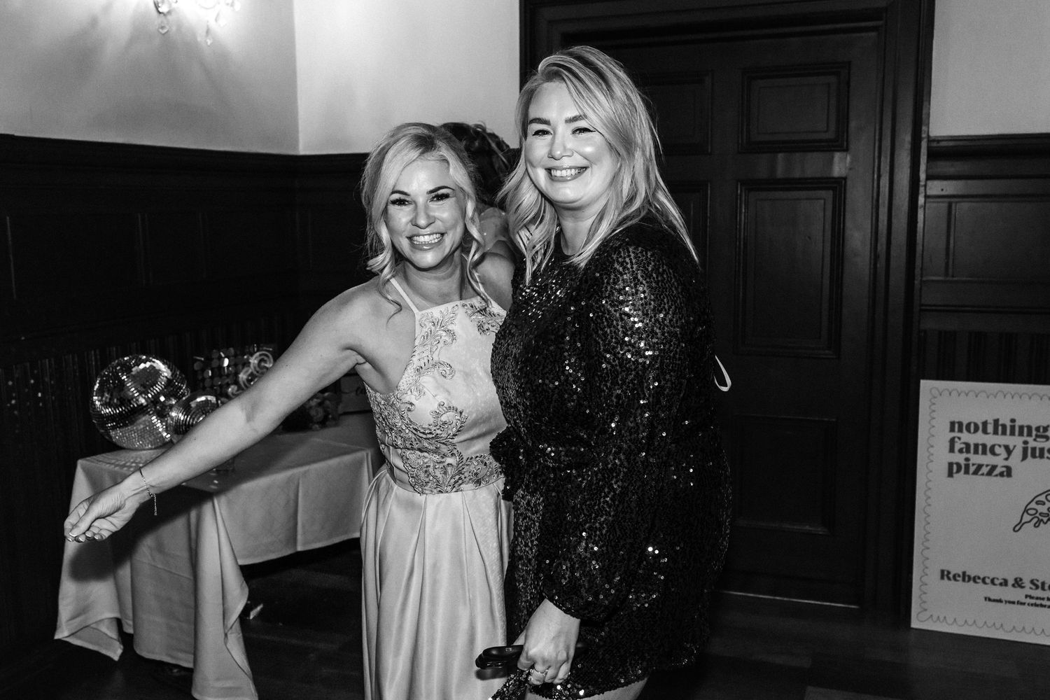 Two women smiling and posing together in black and white photo at a wedding reception.