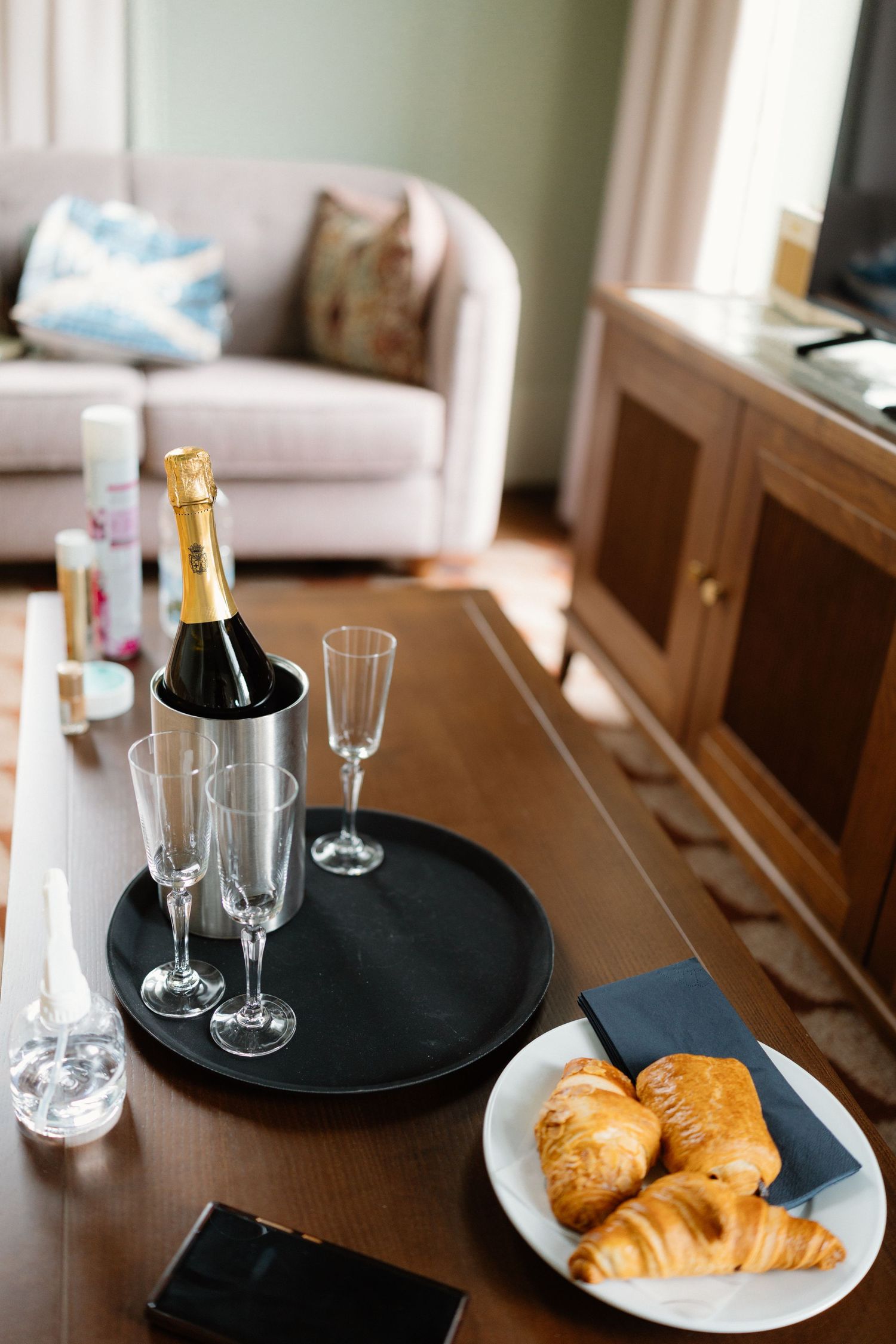 Champagne bottle in ice bucket with flutes and croissants on a wooden table in an elegant hotel room.