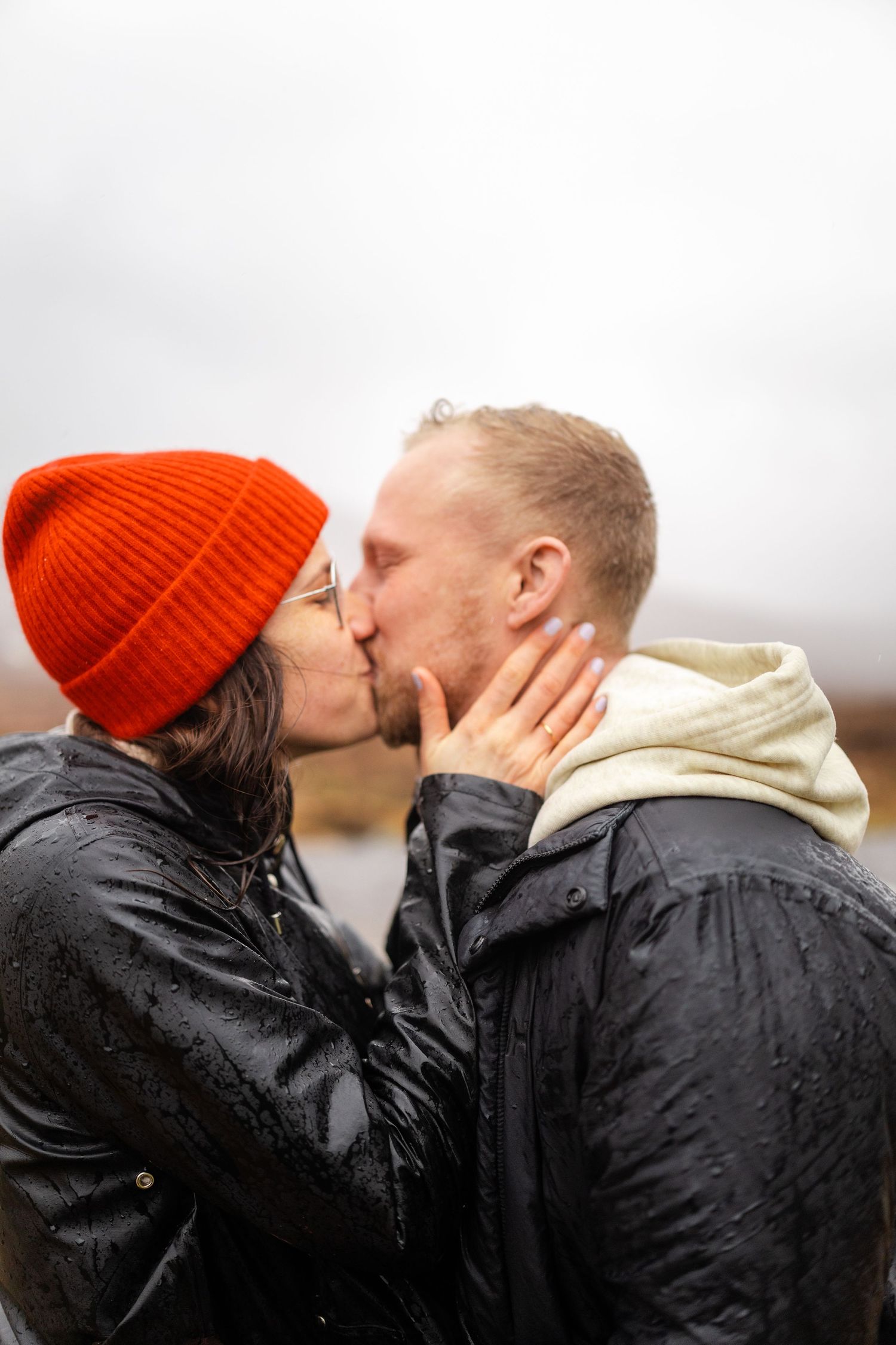 A couple in winter coats sharing an intimate moment against a misty outdoor backdrop.