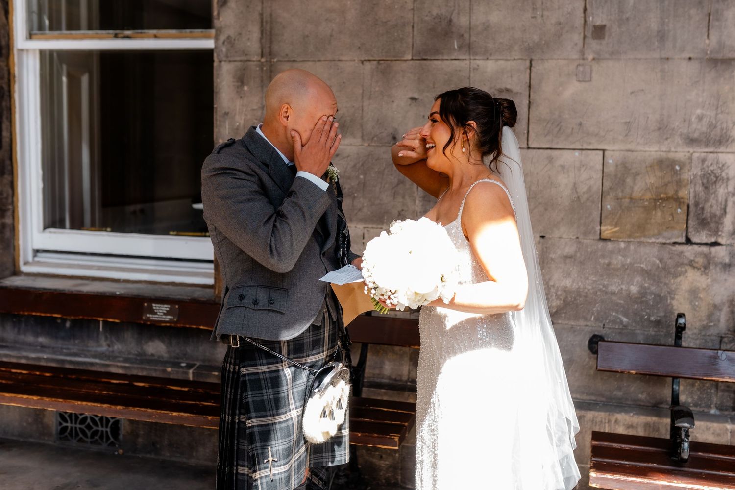 Wedding couple shares intimate moment against stone wall backdrop.