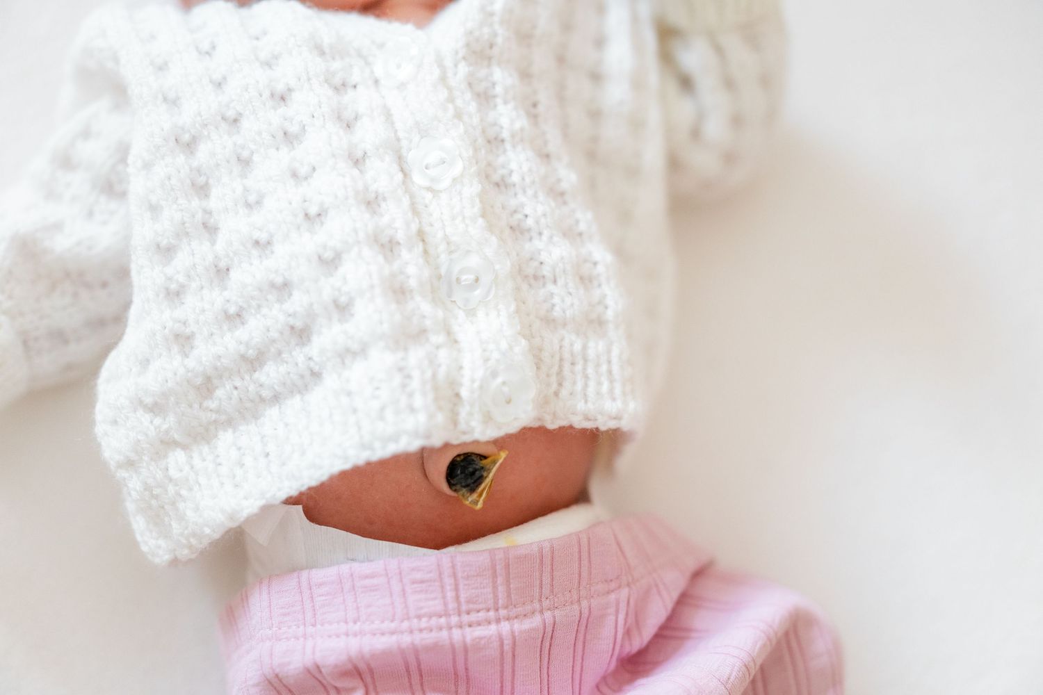 Baby wearing a white knit sweater and pink pants lies on a white surface.