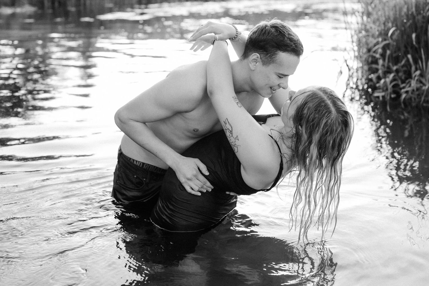 A romantic couple embraces in a lake with water splashing around them in black and white.