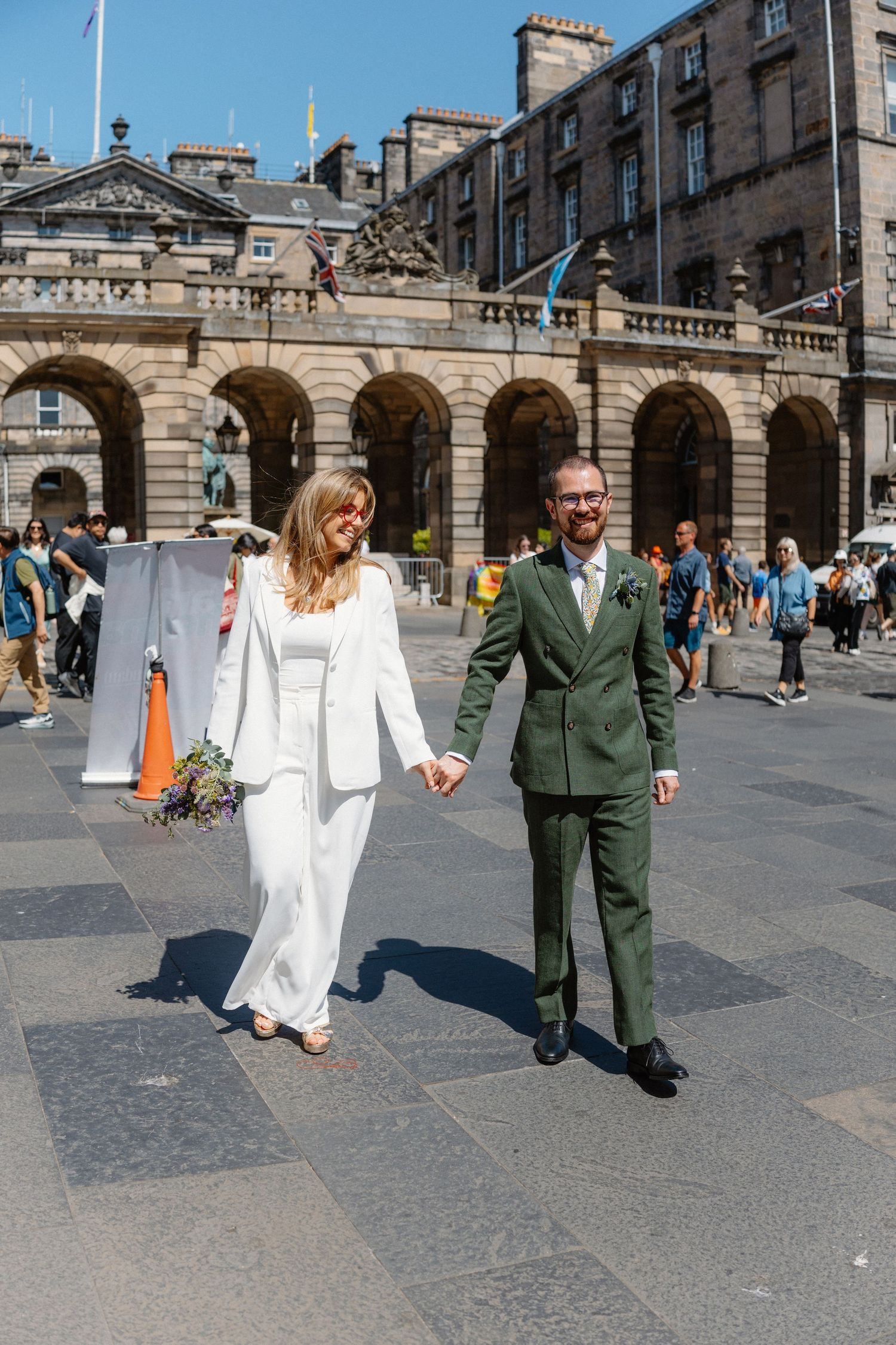 Couple walking together on cobblestone plaza in front of historic Edinburgh architecture.