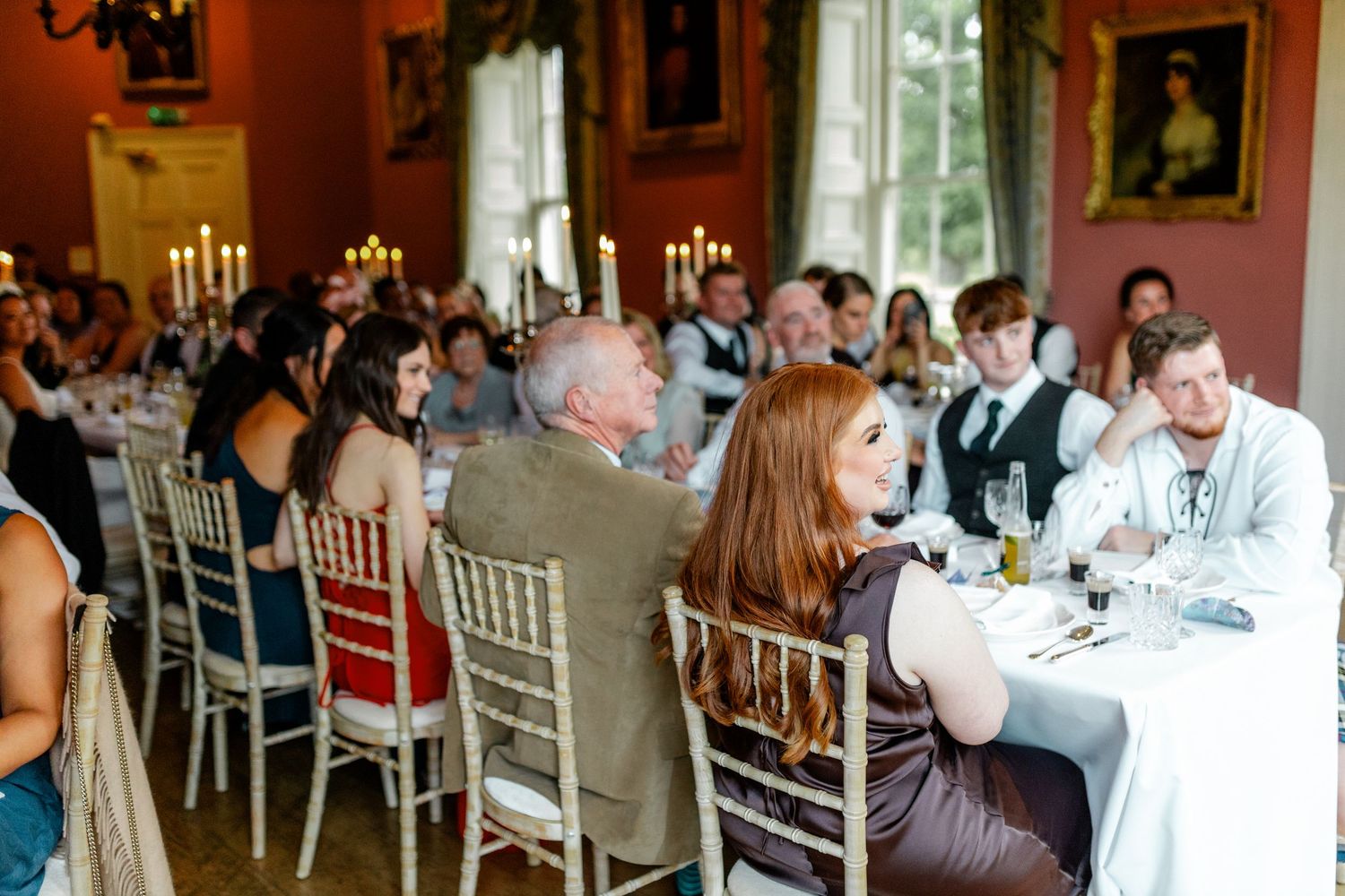 Wedding guests seated at elegant tables in a reception hall with pink walls and ornate decor.