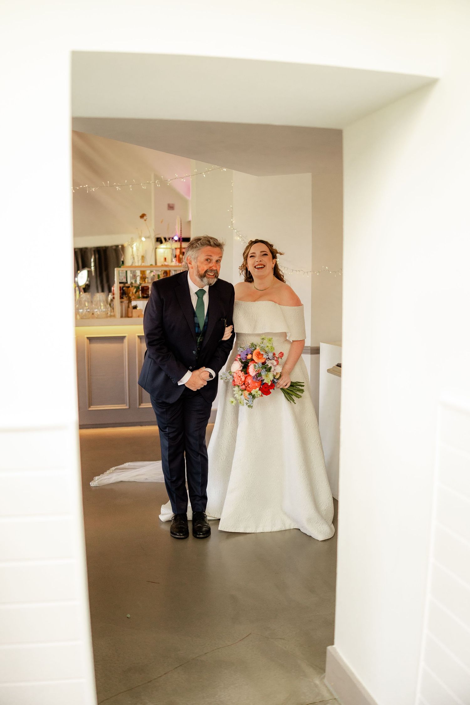 A tender moment between a bride in white and her escort walking down a light-filled hallway.