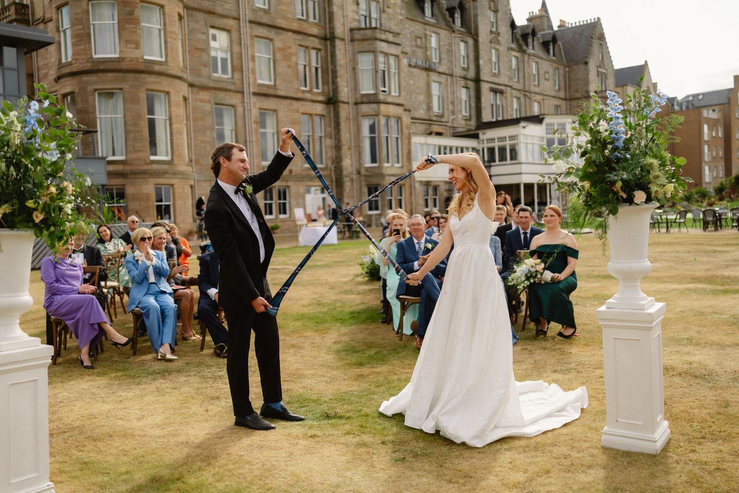 Bride and groom celebrating outdoor wedding ceremony at elegant Scottish manor with seated guests.