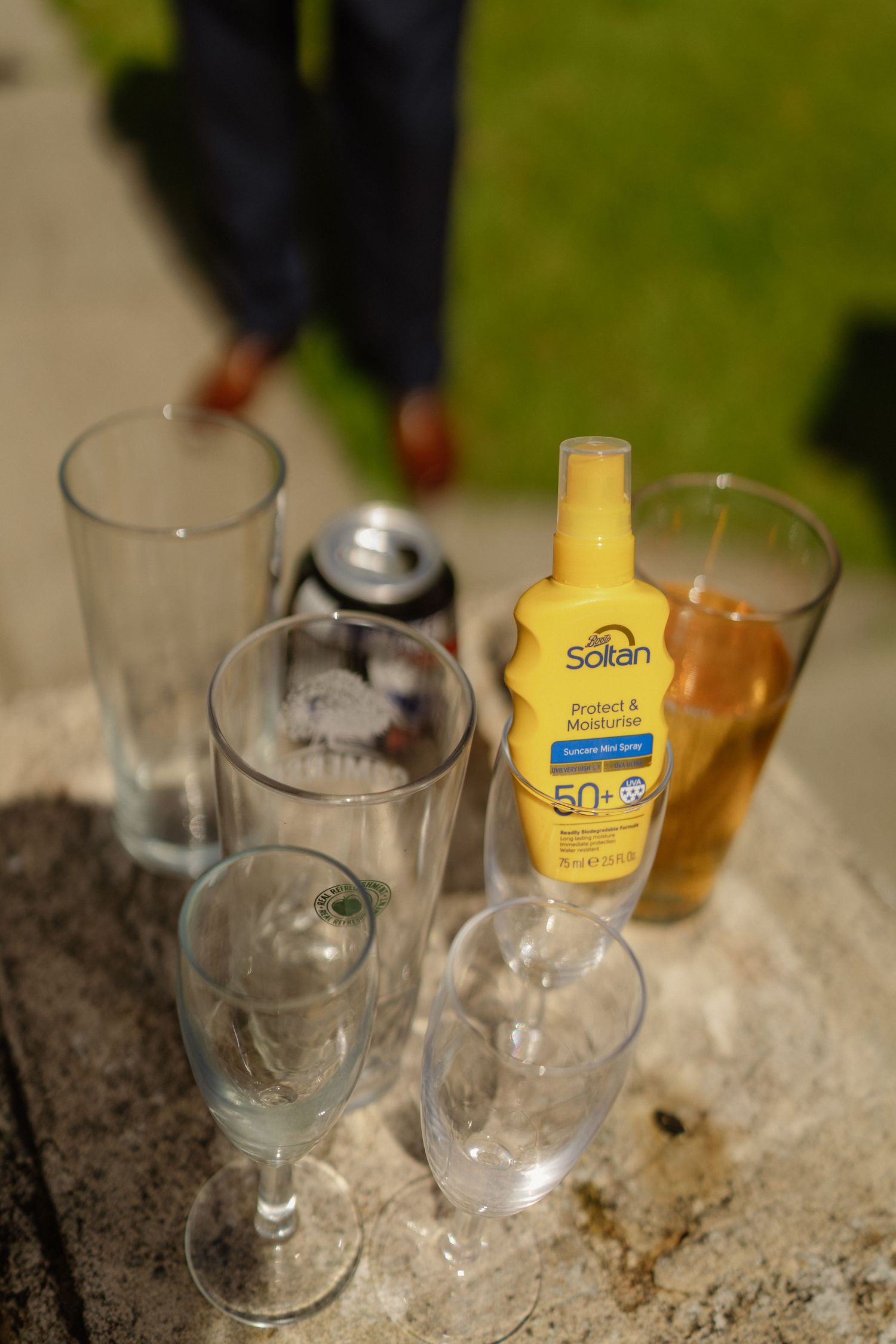 Wedding reception glasses and Soltan SPF50 sunscreen on stone wall outdoors.