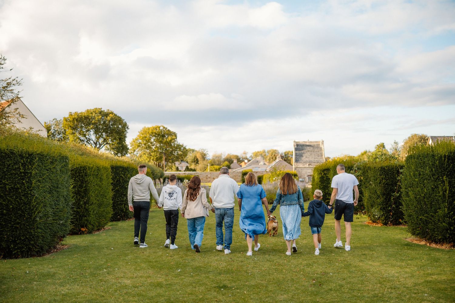 Group walking together along garden path with tall hedges on sunny day.