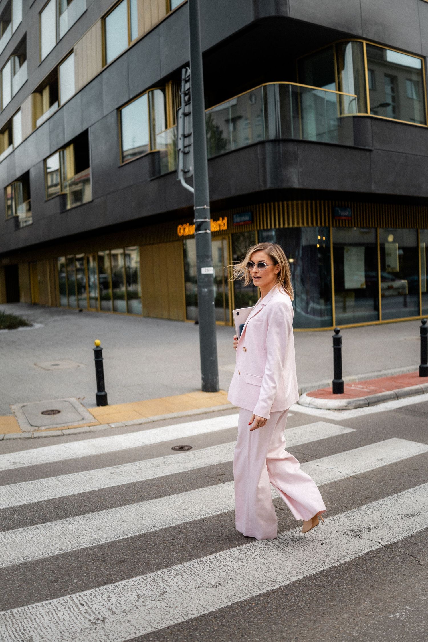Person in light pink suit walking across a pedestrian crossing in an urban setting.