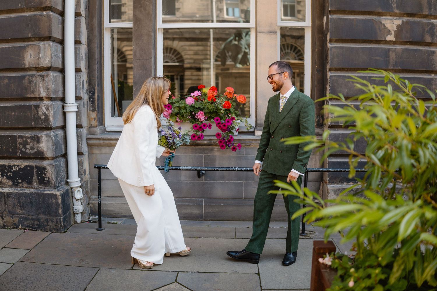 A couple poses for wedding photos on stone steps with floral decorations in an urban setting.