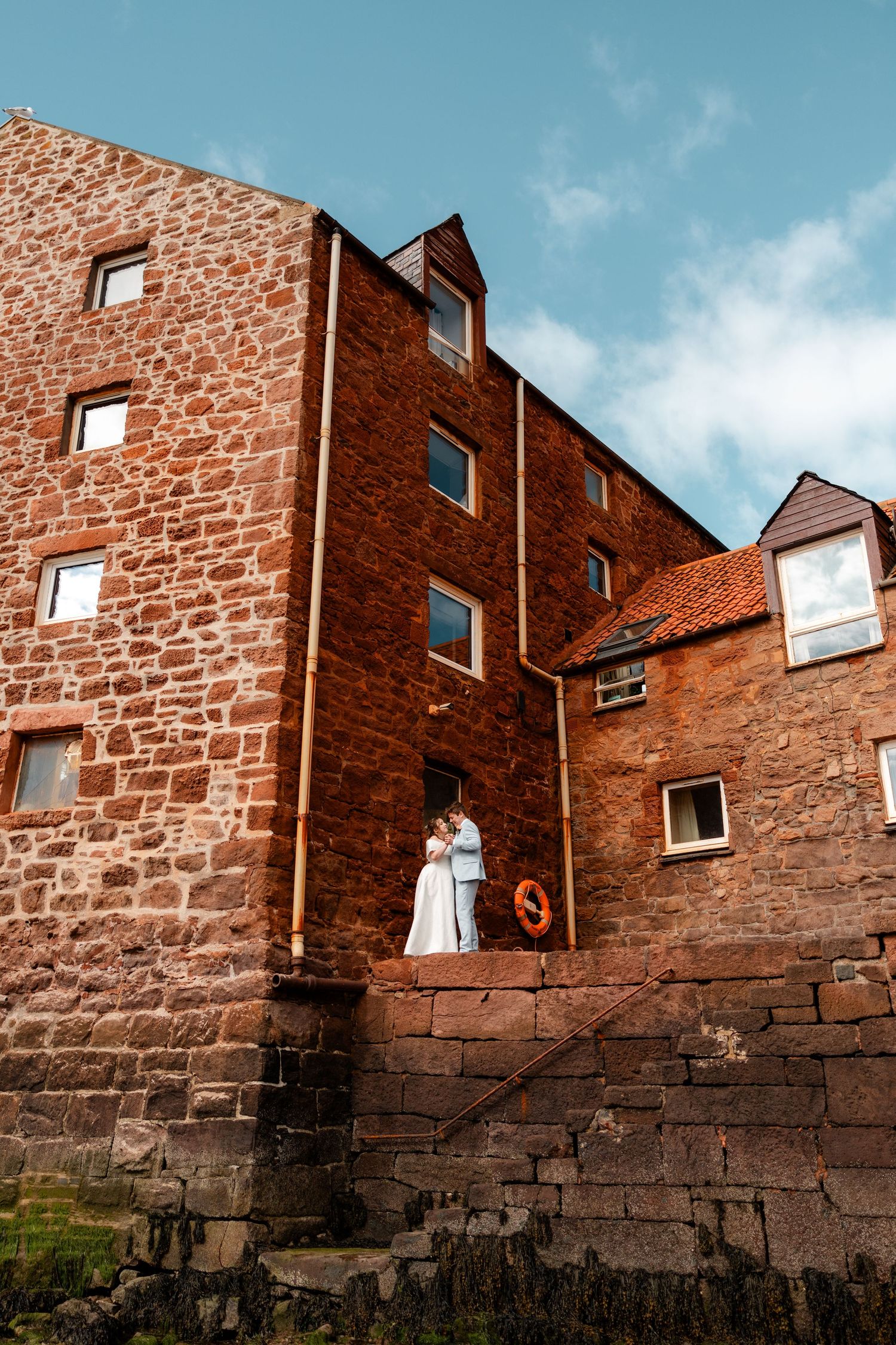 Red brick buildings with windows rise above an old stone wall under a blue sky.