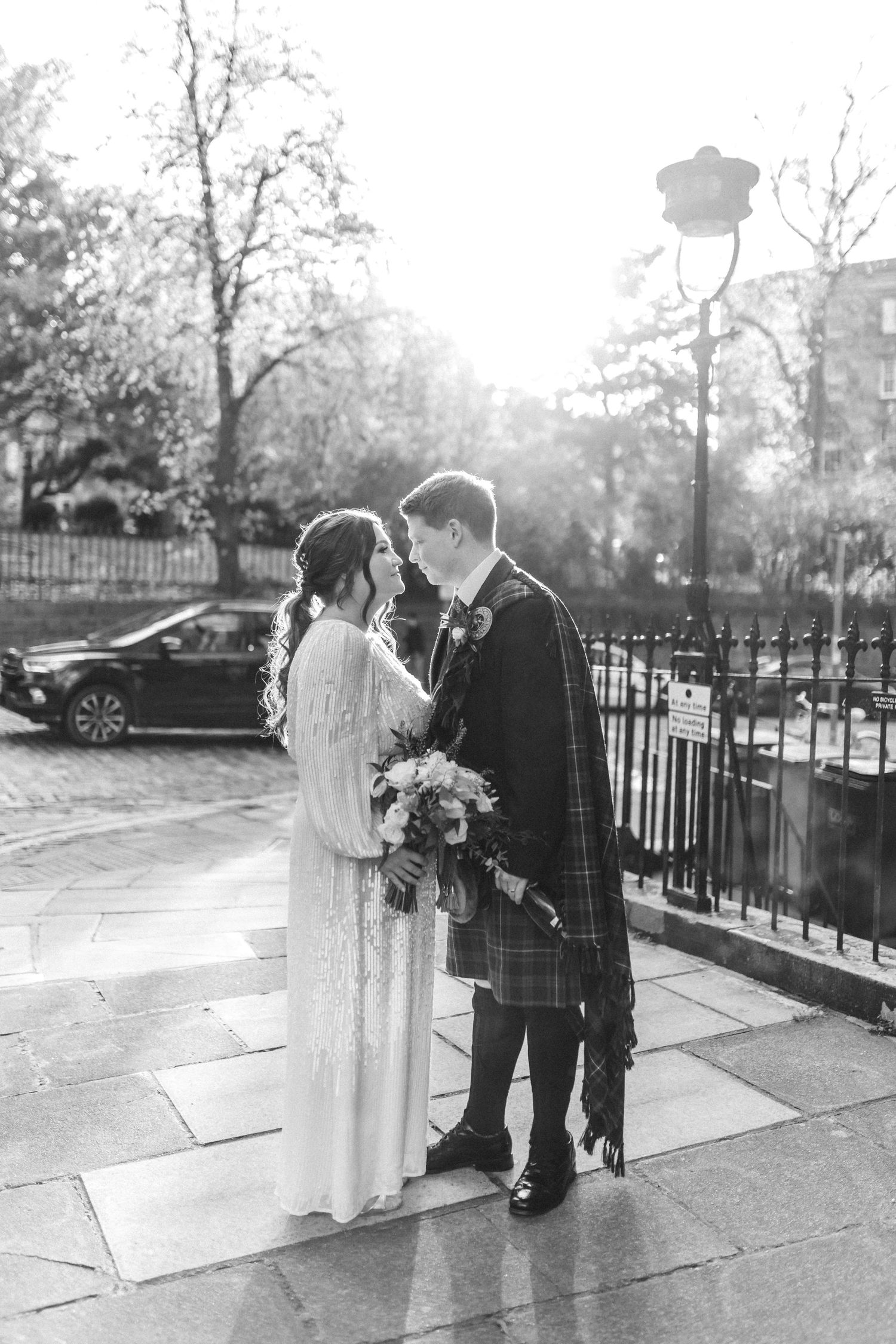 Wedding couple in black and white photography standing on a sidewalk with iron railings.