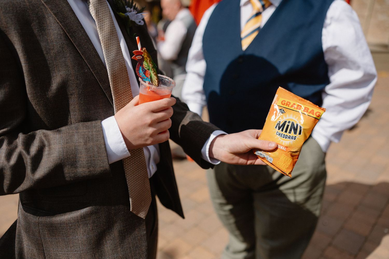 Close-up of wedding guest holding beverage and snack at outdoor reception.
