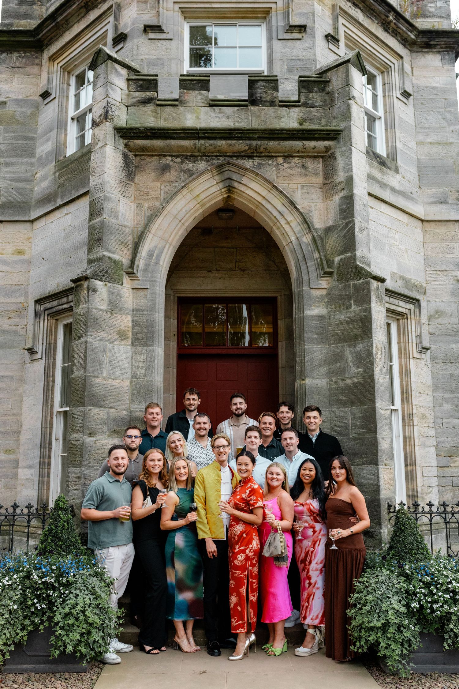 Large group photo of wedding guests posing outside a grand stone building entrance.