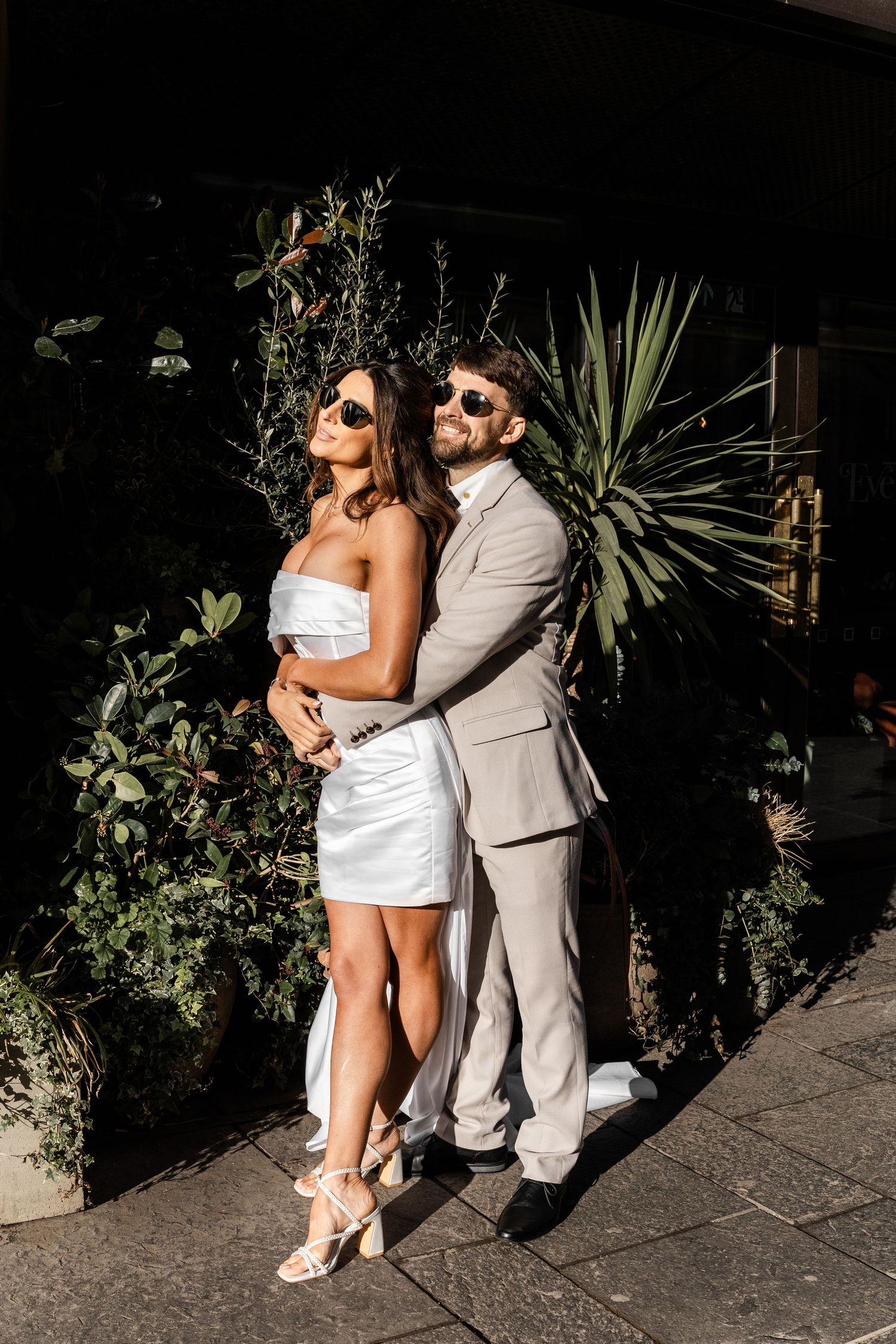 Couple embraces in front of lush greenery and plants at night.
