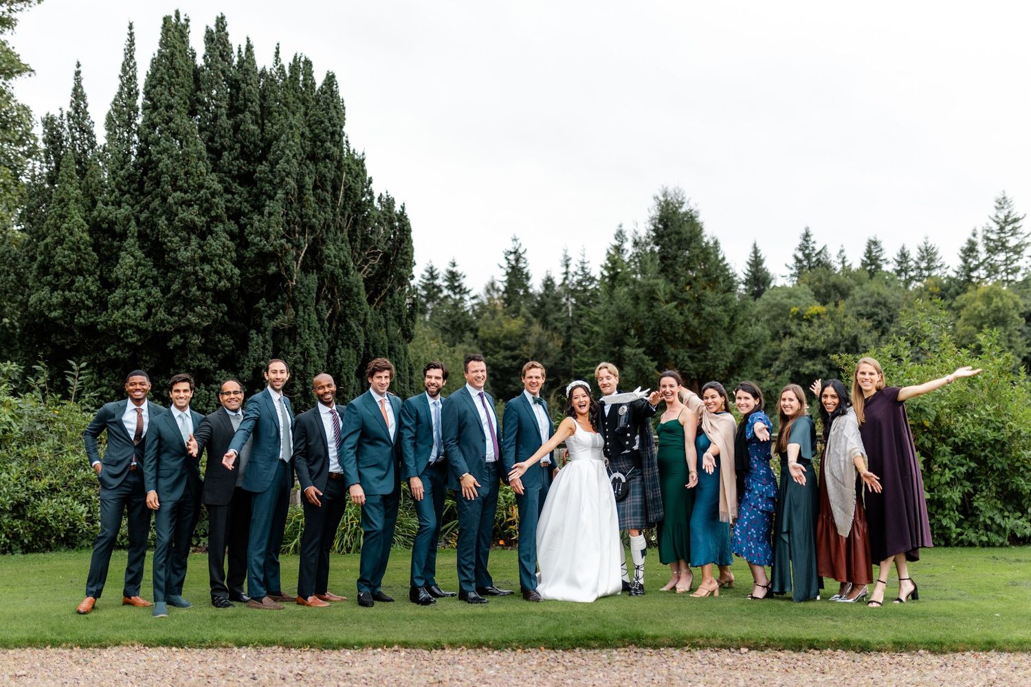Wedding party members stand in line against backdrop of tall cypress trees.