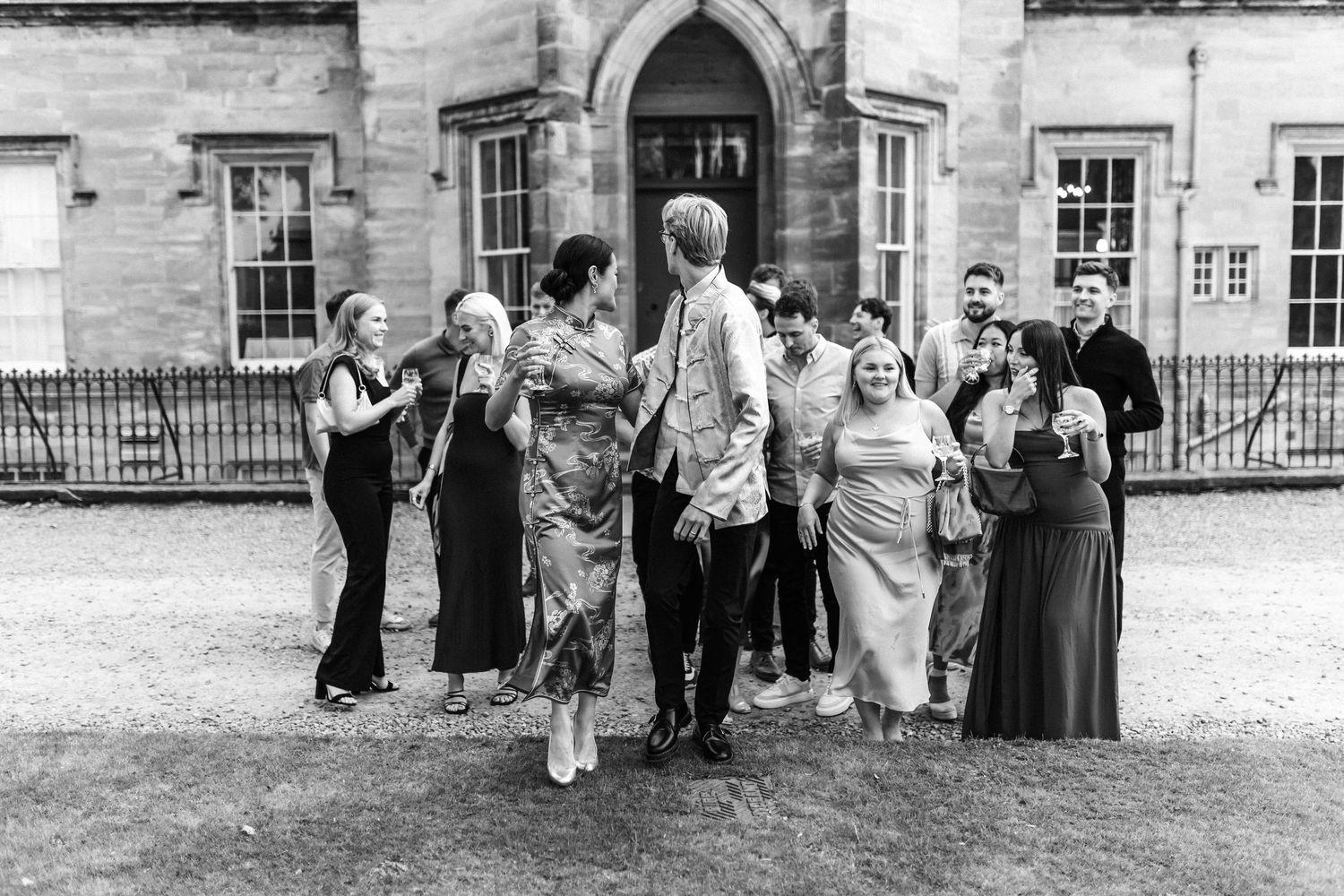 Black and white photo of wedding guests posed in front of a historic stone building.