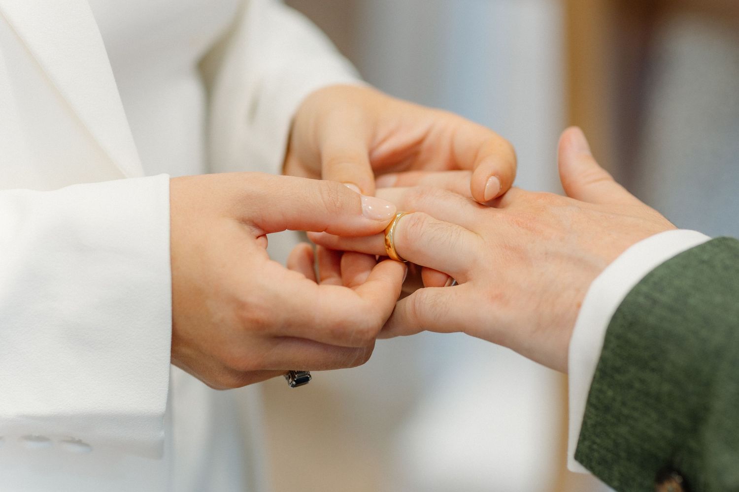 Close-up of bride placing gold wedding ring on grooms finger during ceremony.