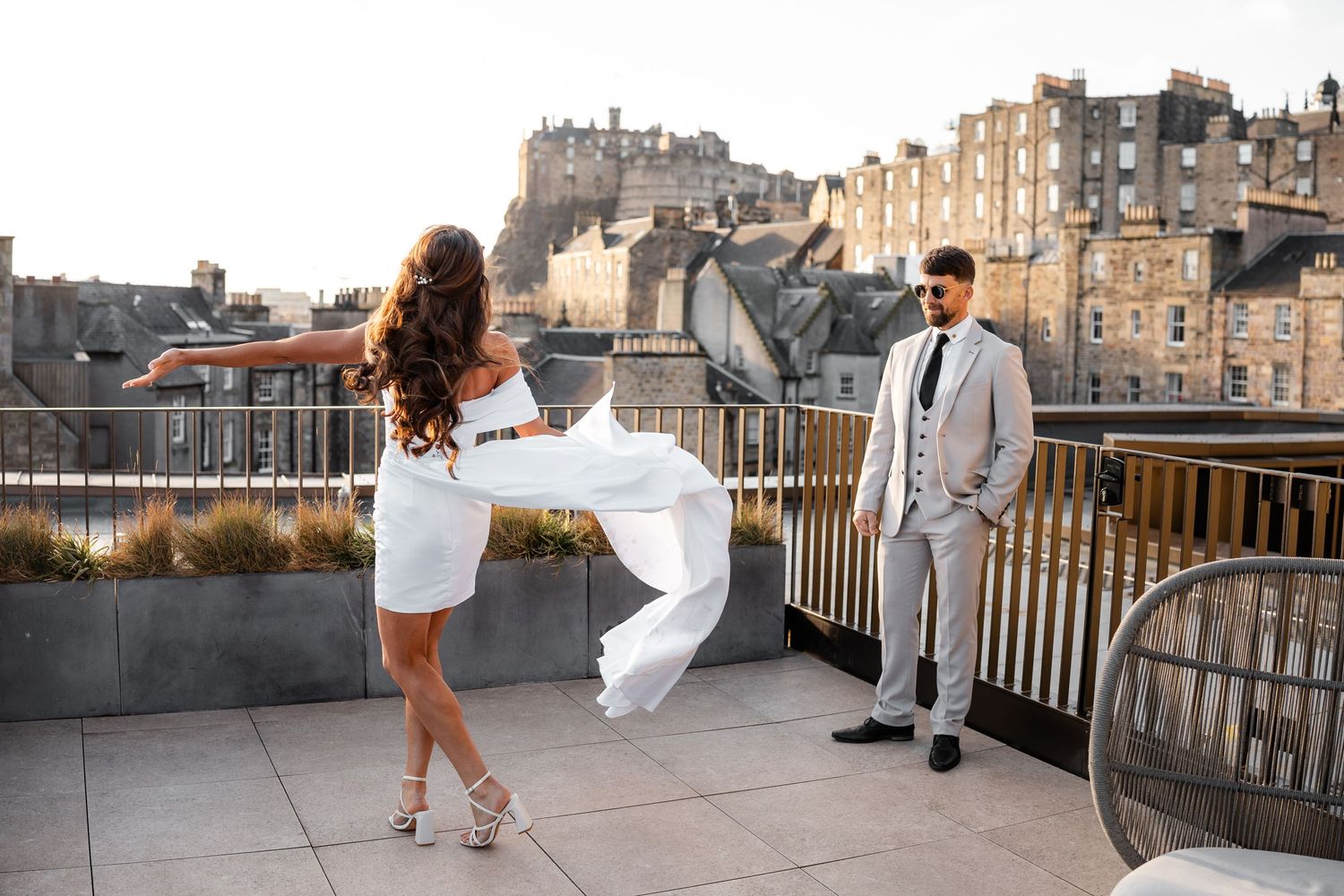 Newlyweds enjoying playful moments on a city rooftop during sunset.