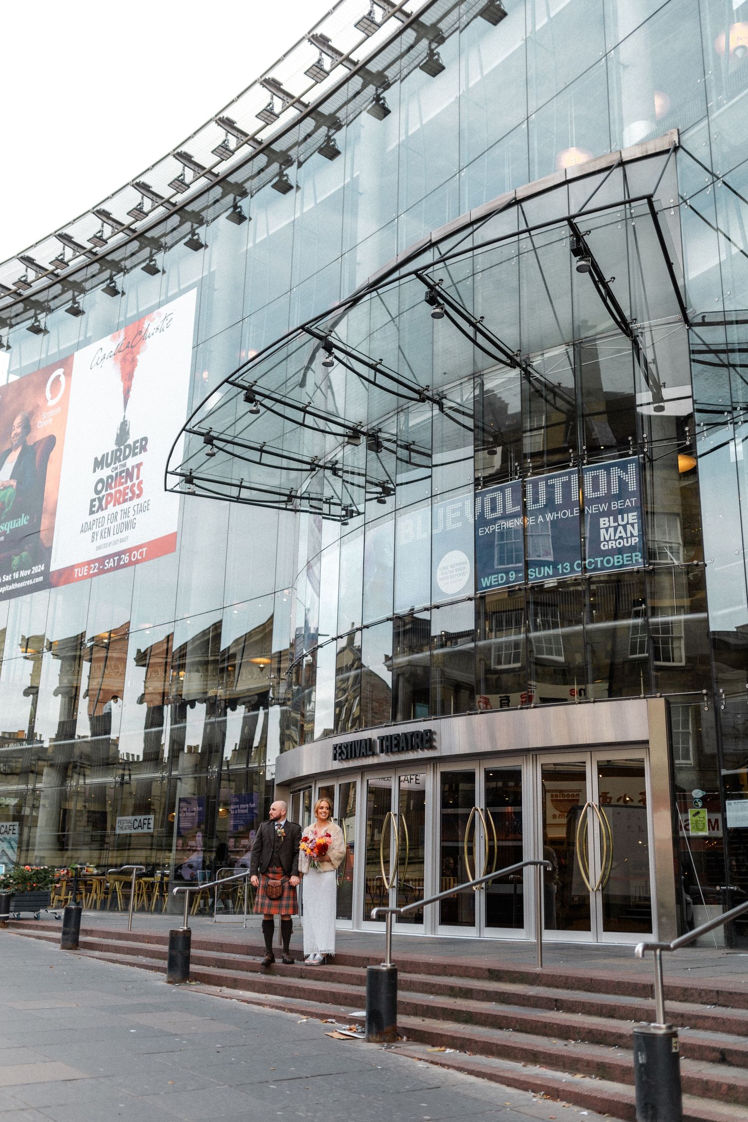 Modern glass facade of Edinburgh's Festival Theatre with promotional banners and steps.