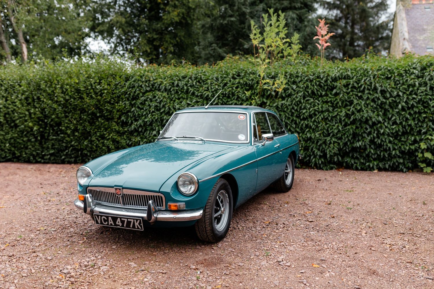 Vintage teal MG classic car displayed on a garden driveway.