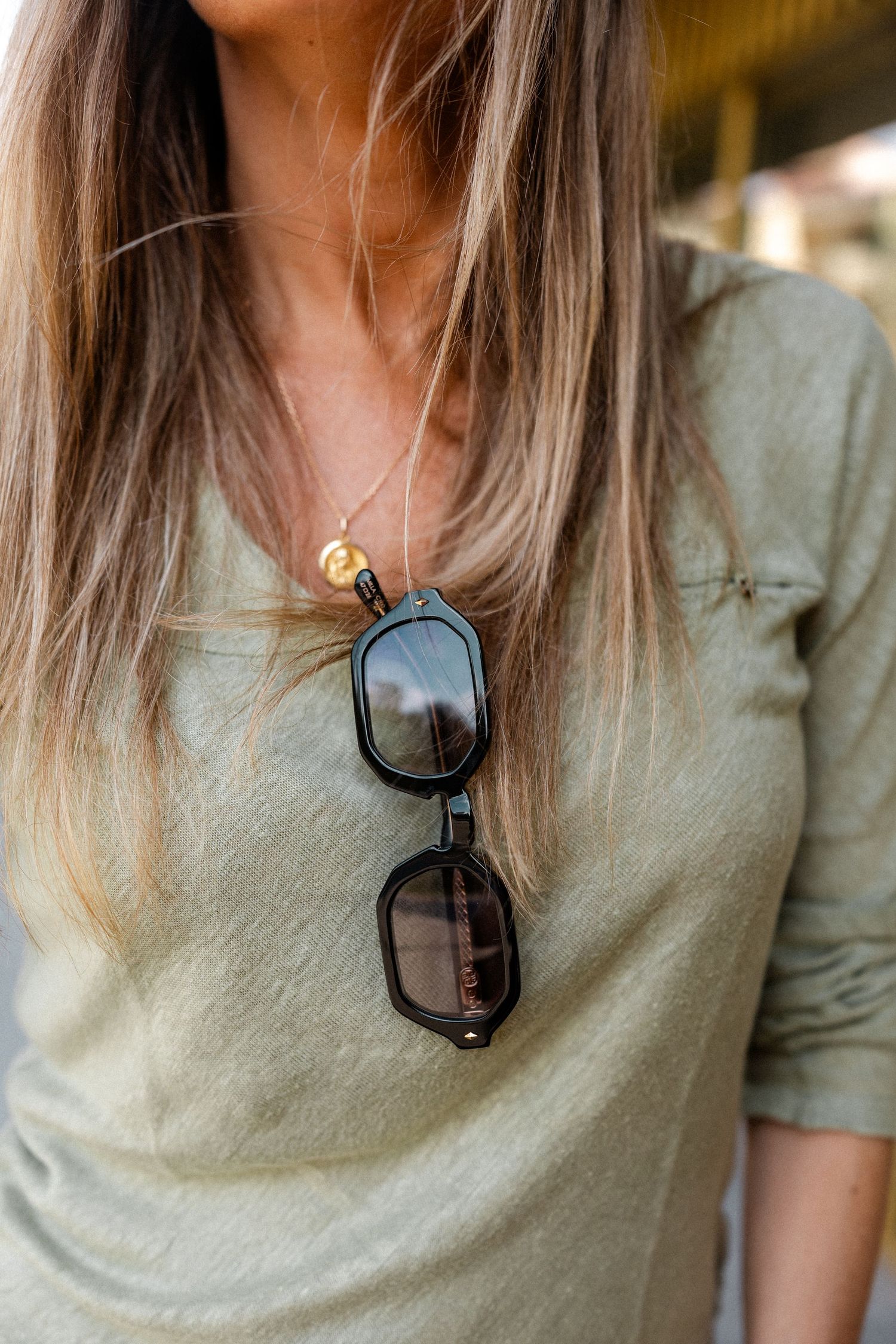 Close-up detail shots of sage green shirt and sunglasses necklace.