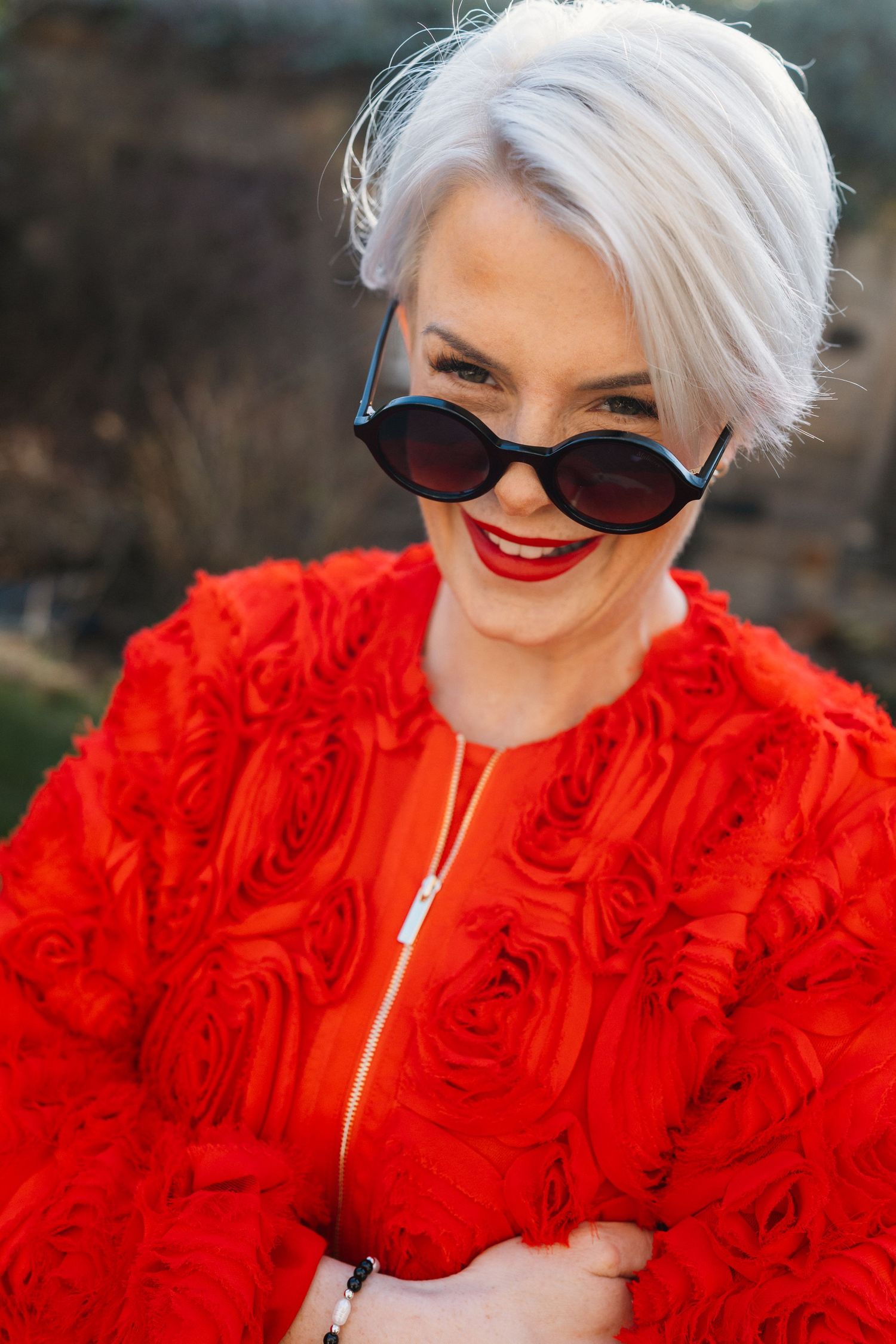 Person with platinum hair and red ruffled dress poses in a series of glamorous outdoor shots against a dark background.