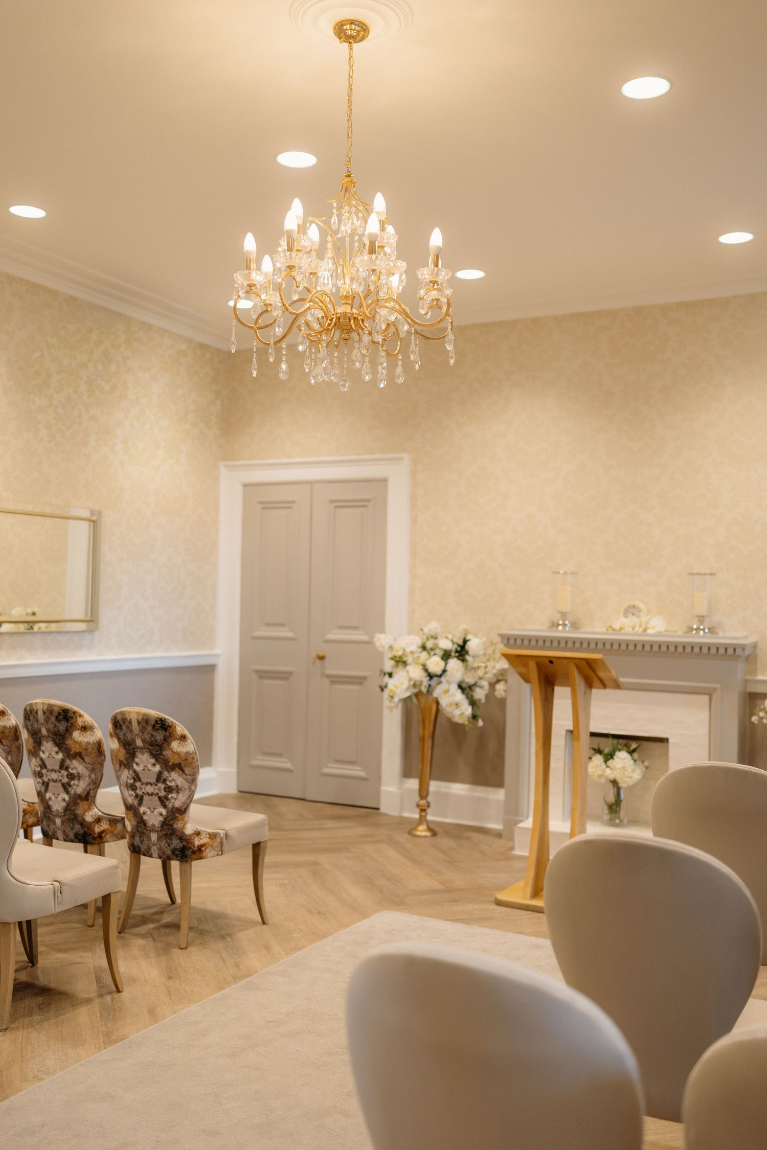 Elegant wedding ceremony room with gold chandelier, floral arrangements, and ornate chairs in a cream and gold interior.