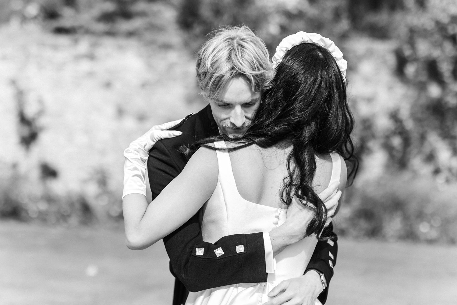 Black and white photo of a couple embracing tenderly at an outdoor wedding ceremony.