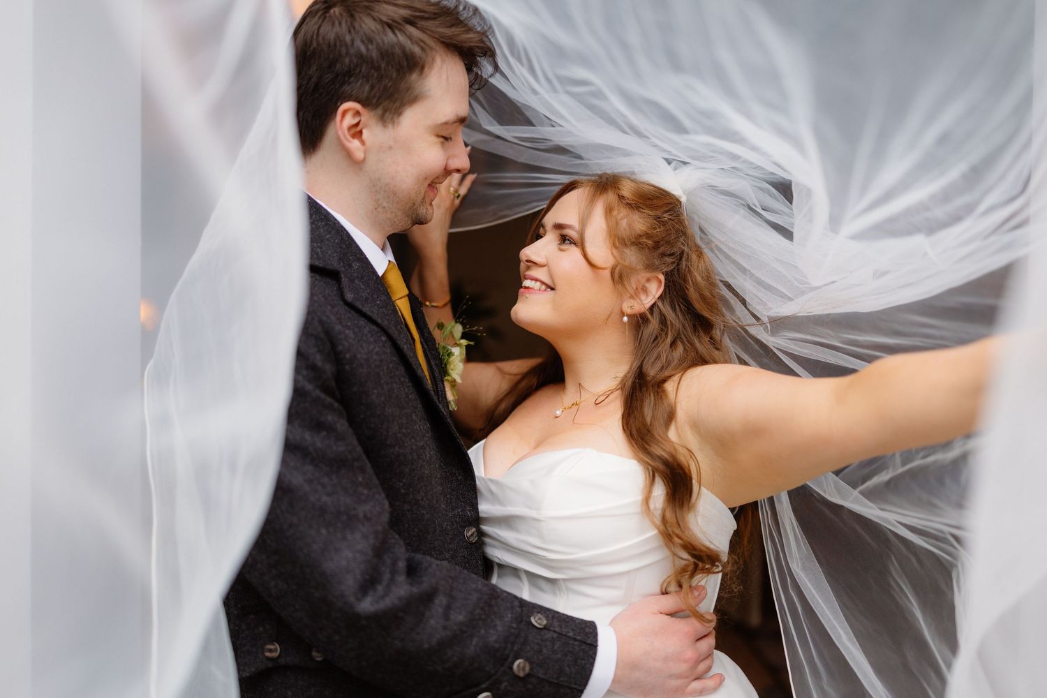 Romantic bride and groom portrait with flowing veil surrounding them during outdoor wedding photos.