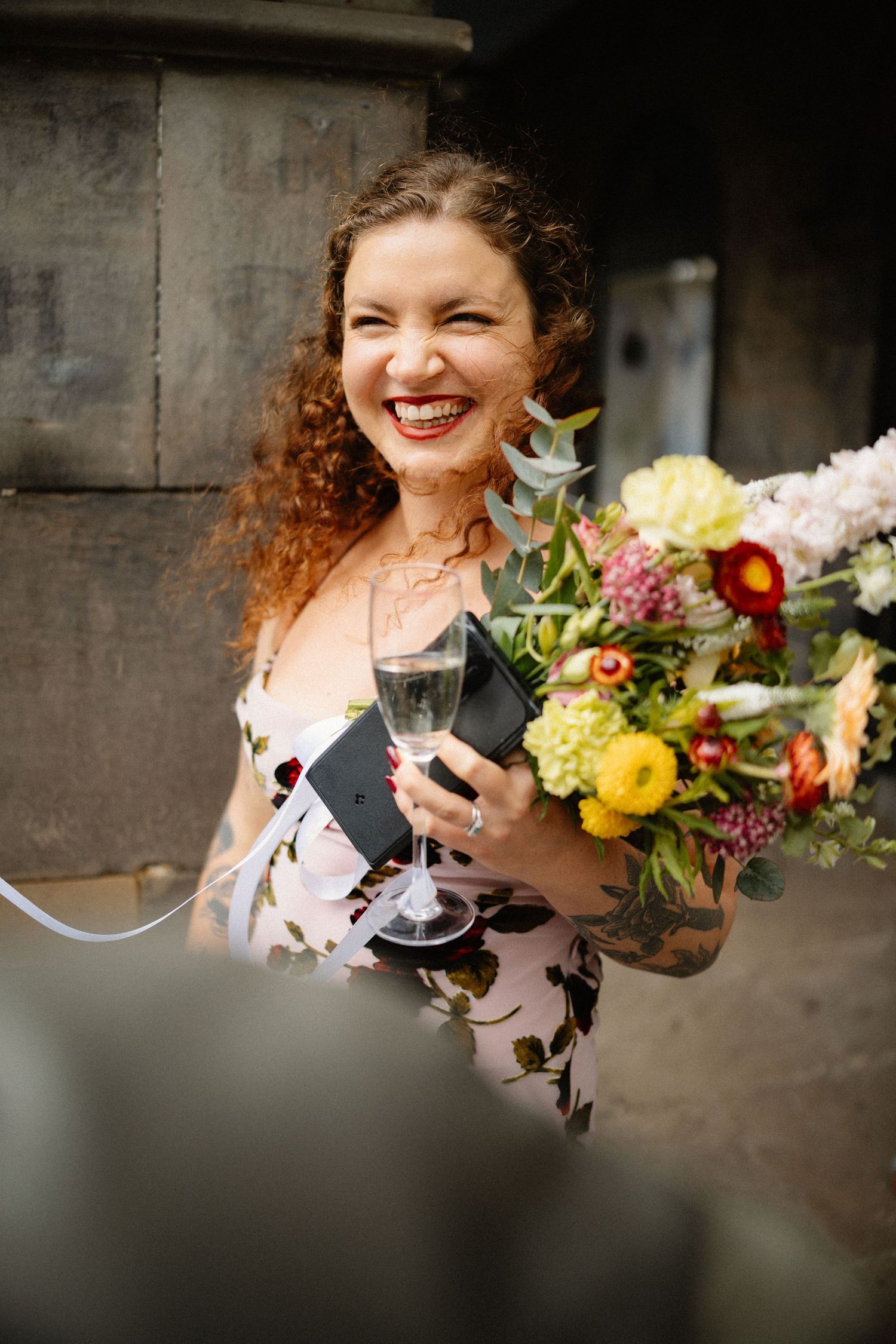 Joyful bride laughing holding champagne glass and colorful bouquet.