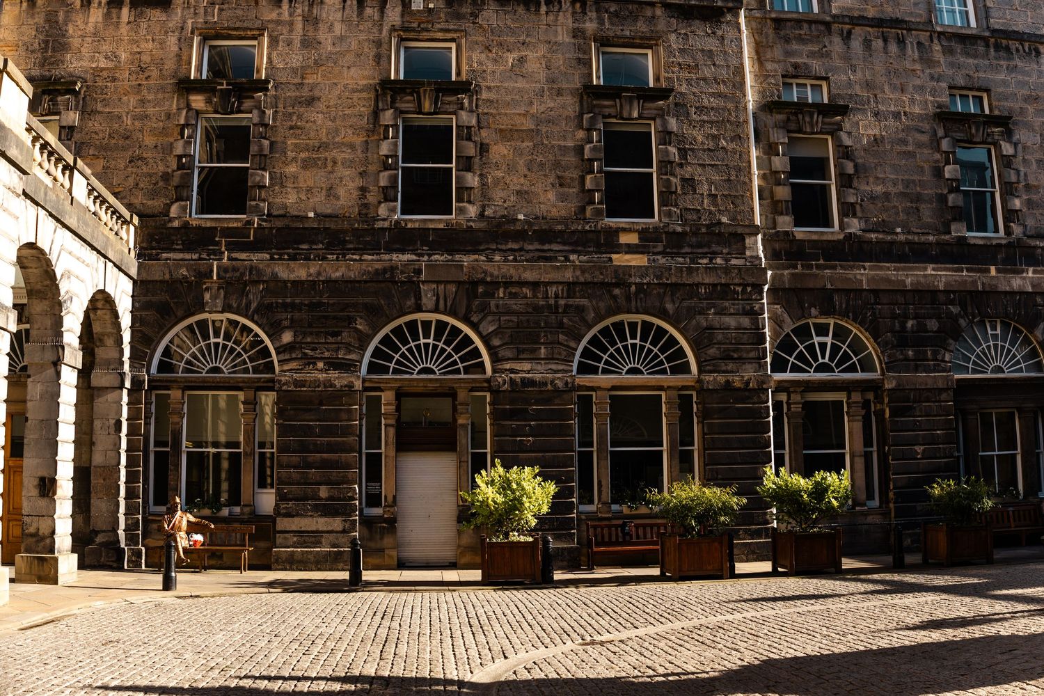 Historic stone building facade with arched windows and cobblestone street in Edinburgh.