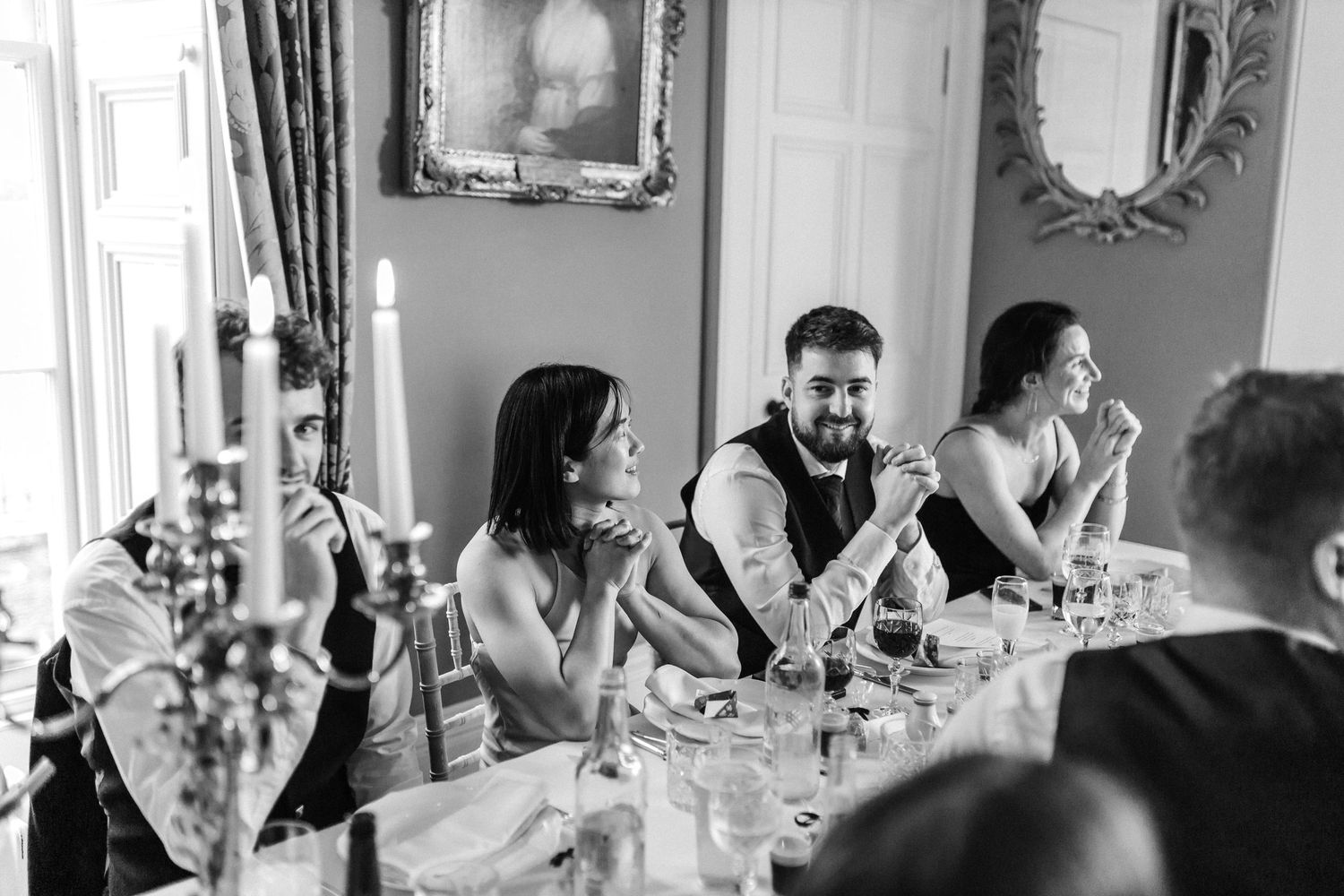 Black and white photo of wedding guests laughing during dinner speeches.