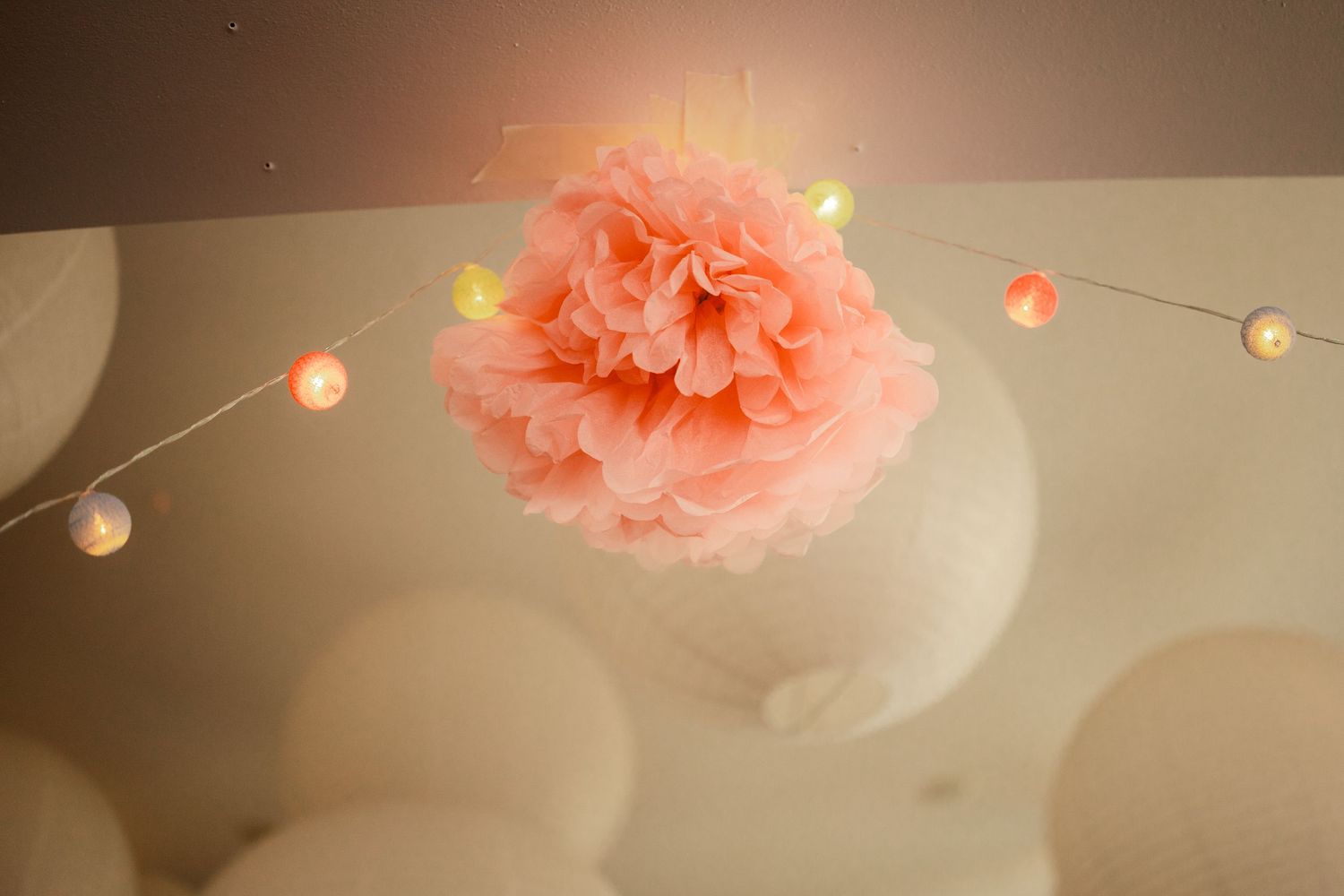Soft pink paper lanterns and string lights create a romantic ambiance against a warm beige background.