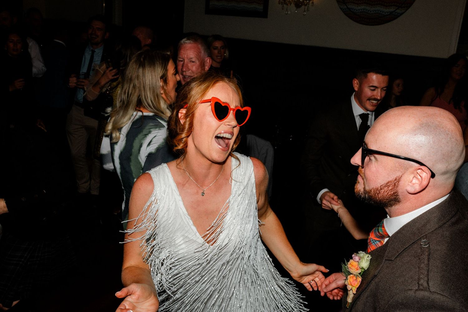 Wedding guests dancing and laughing during an energetic reception celebration.