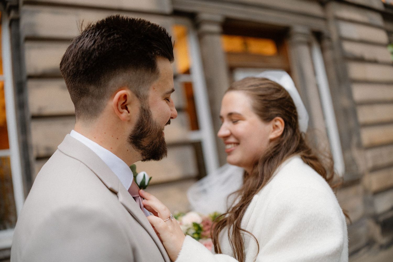 Couple in elegant wedding attire share intimate moments outside a historic stone building.