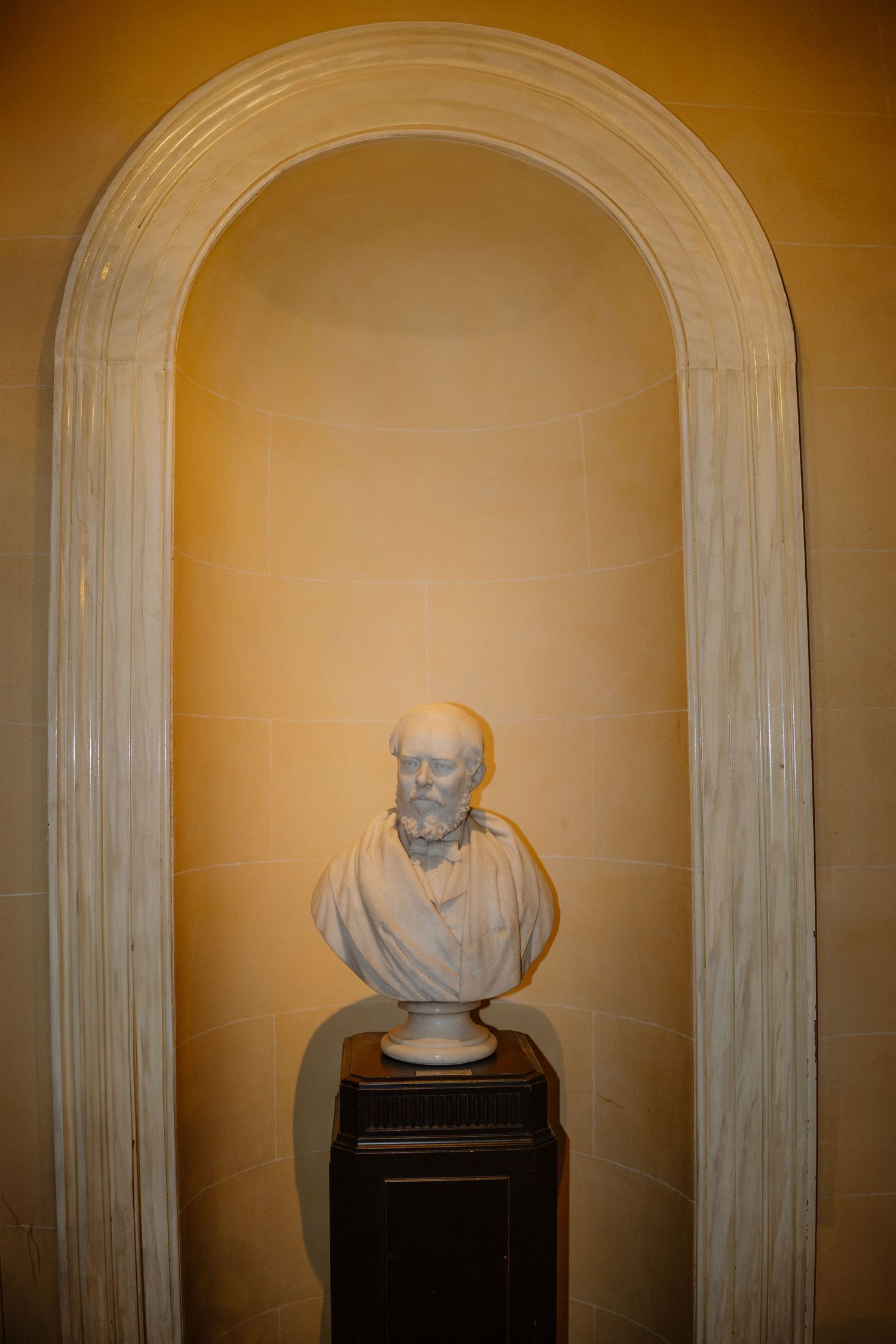 A series of classical marble busts displayed in arched alcoves with warm amber lighting creates an elegant museum gallery setting.